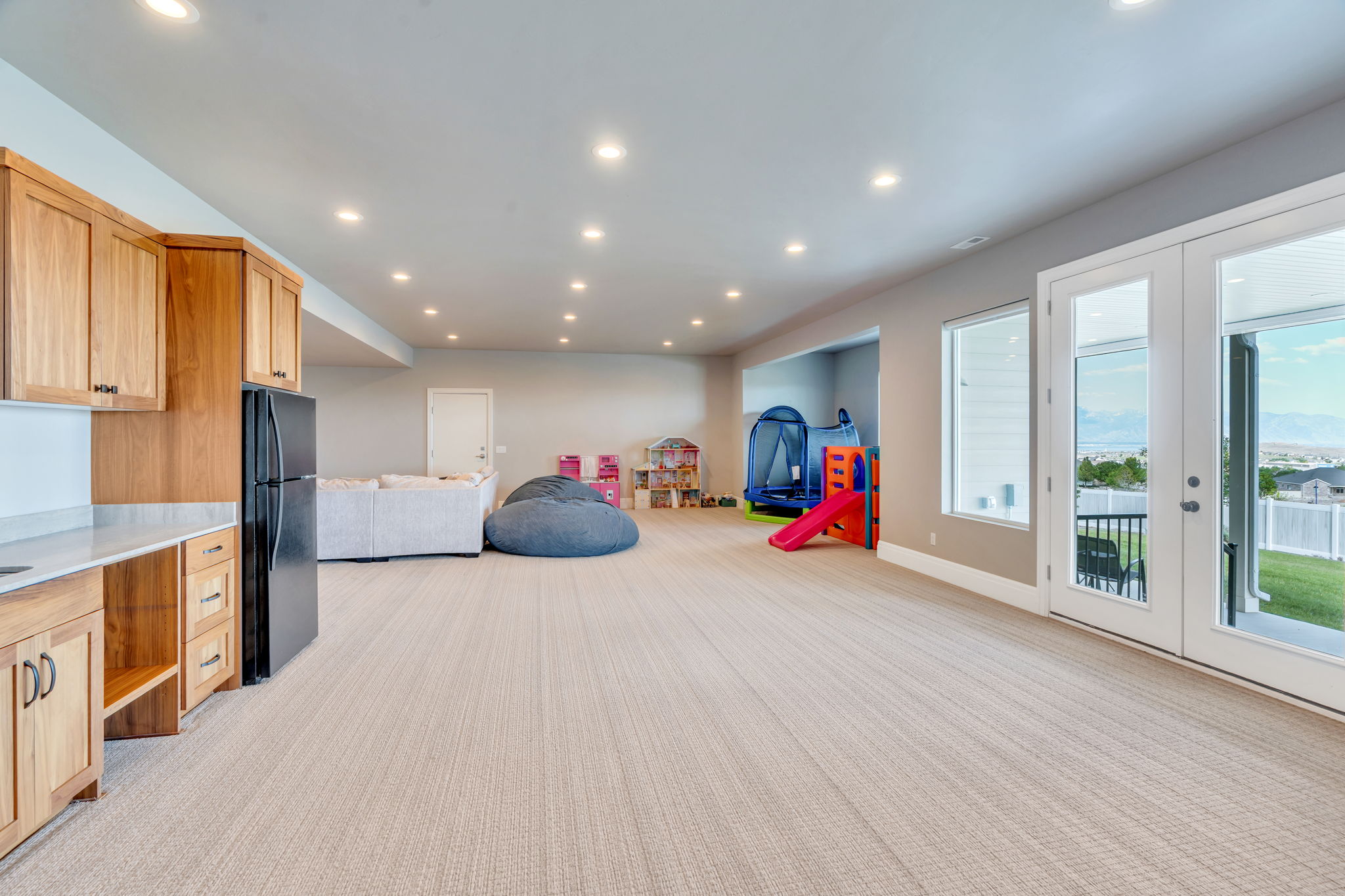 Spacious lower-level area featuring light-toned carpeting, ample recessed lighting, and a built-in wet bar with wood cabinetry and a light-colored countertop