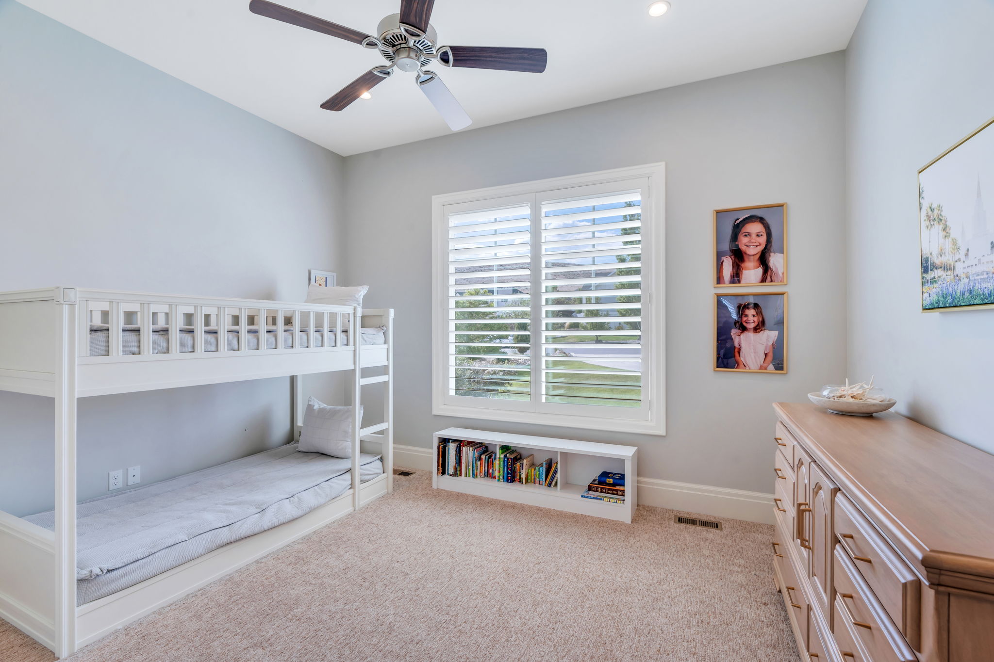 Bright room featuring a large window with white plantation shutters, neutral carpeting, a ceiling fan, recessed lighting, and a built-in bookshelf