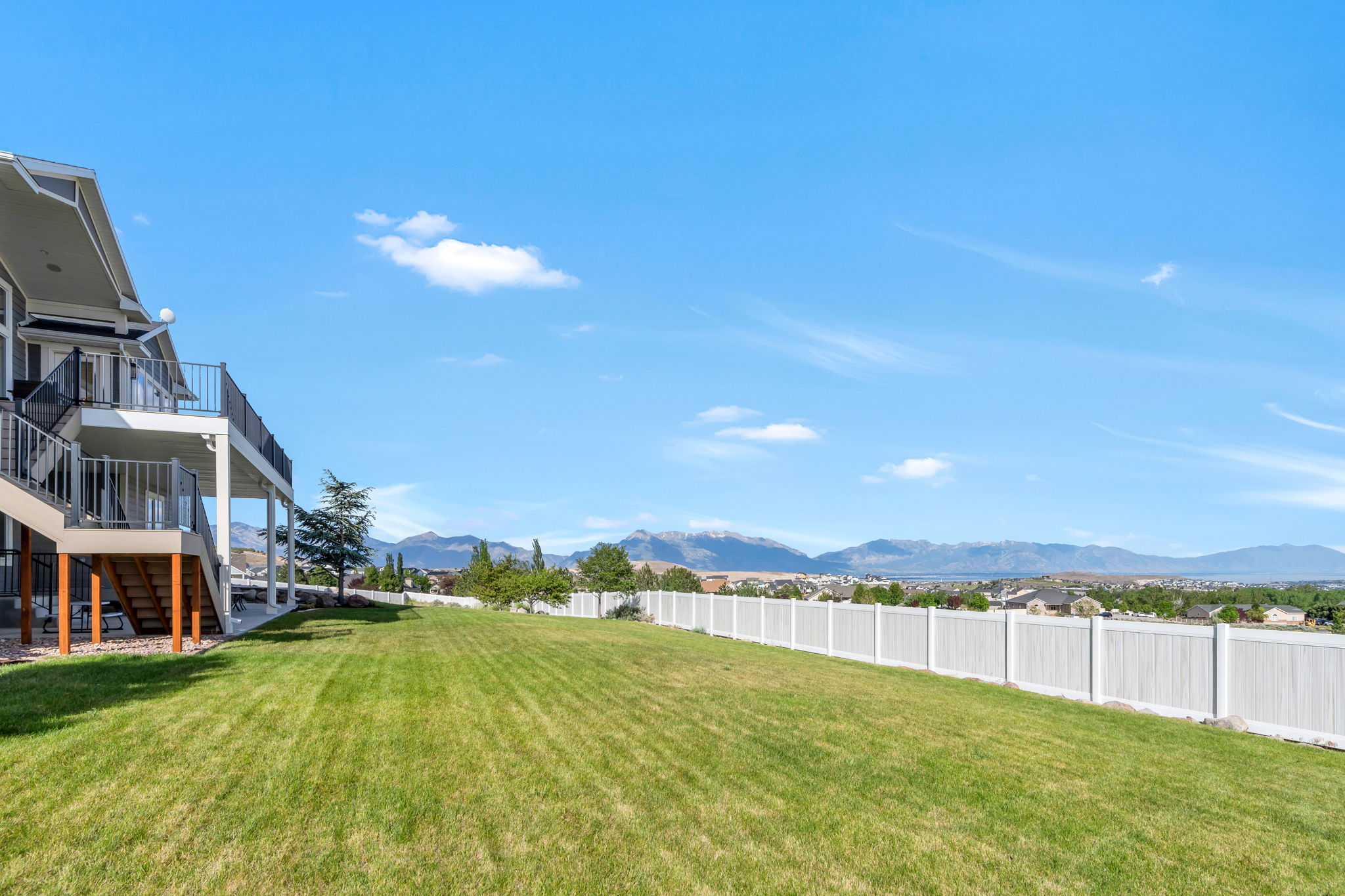 Expansive backyard featuring a manicured lawn, white privacy fence, and mountain scenery