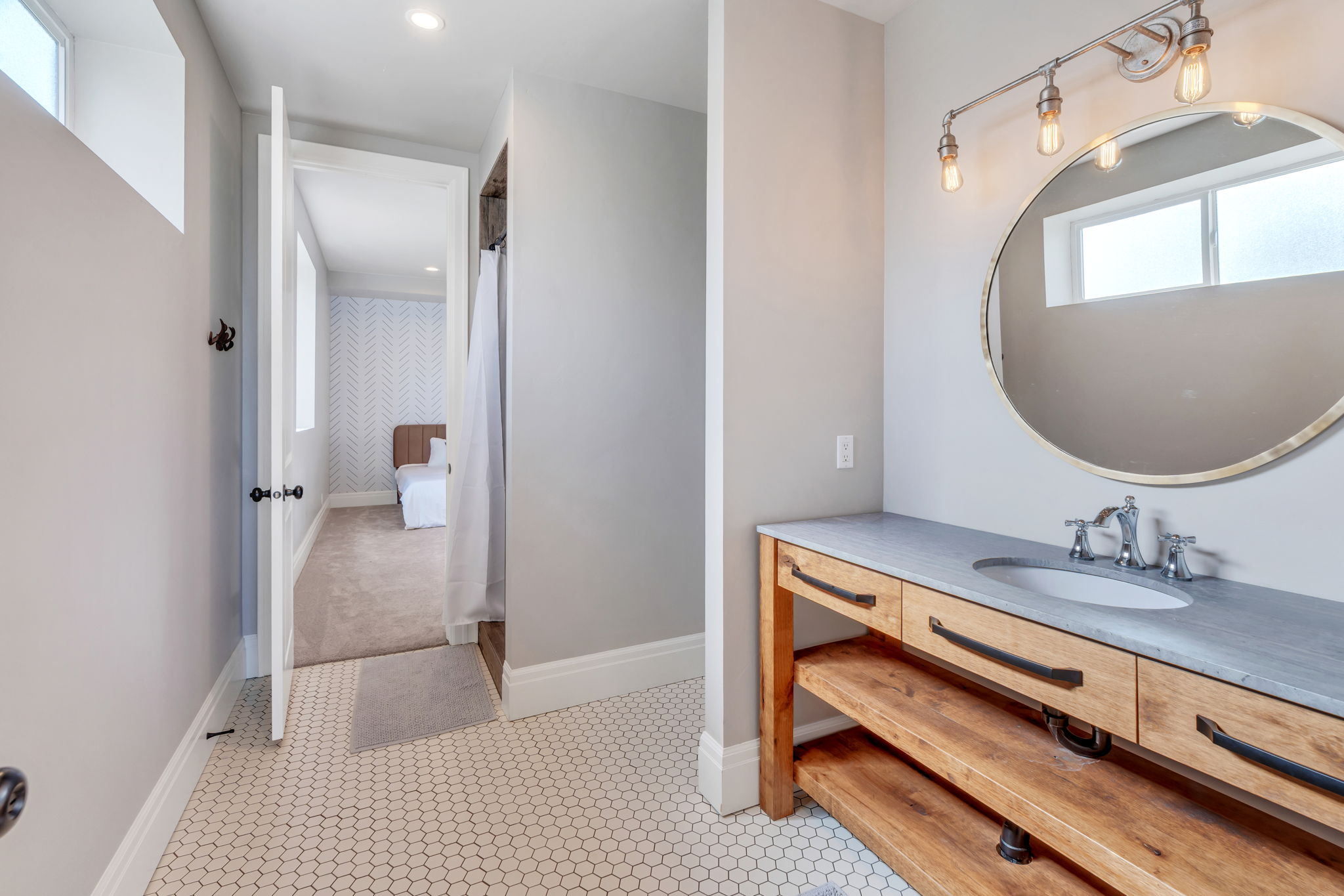 Bathroom featuring a hexagonal tile floor, wood vanity with open shelving and three drawers, undermount sink, and wall-mounted vanity light with exposed bulbs