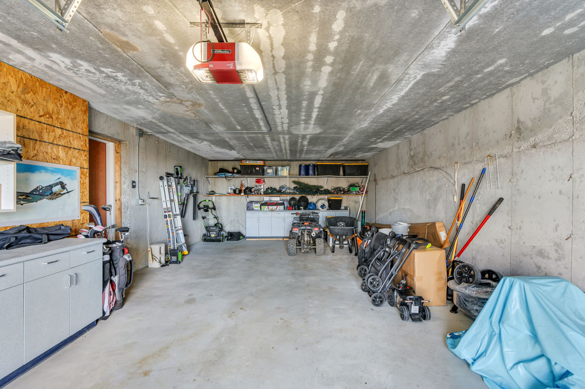 Spacious garage featuring a concrete floor and ceiling, built-in storage shelving, and an automatic garage door opener