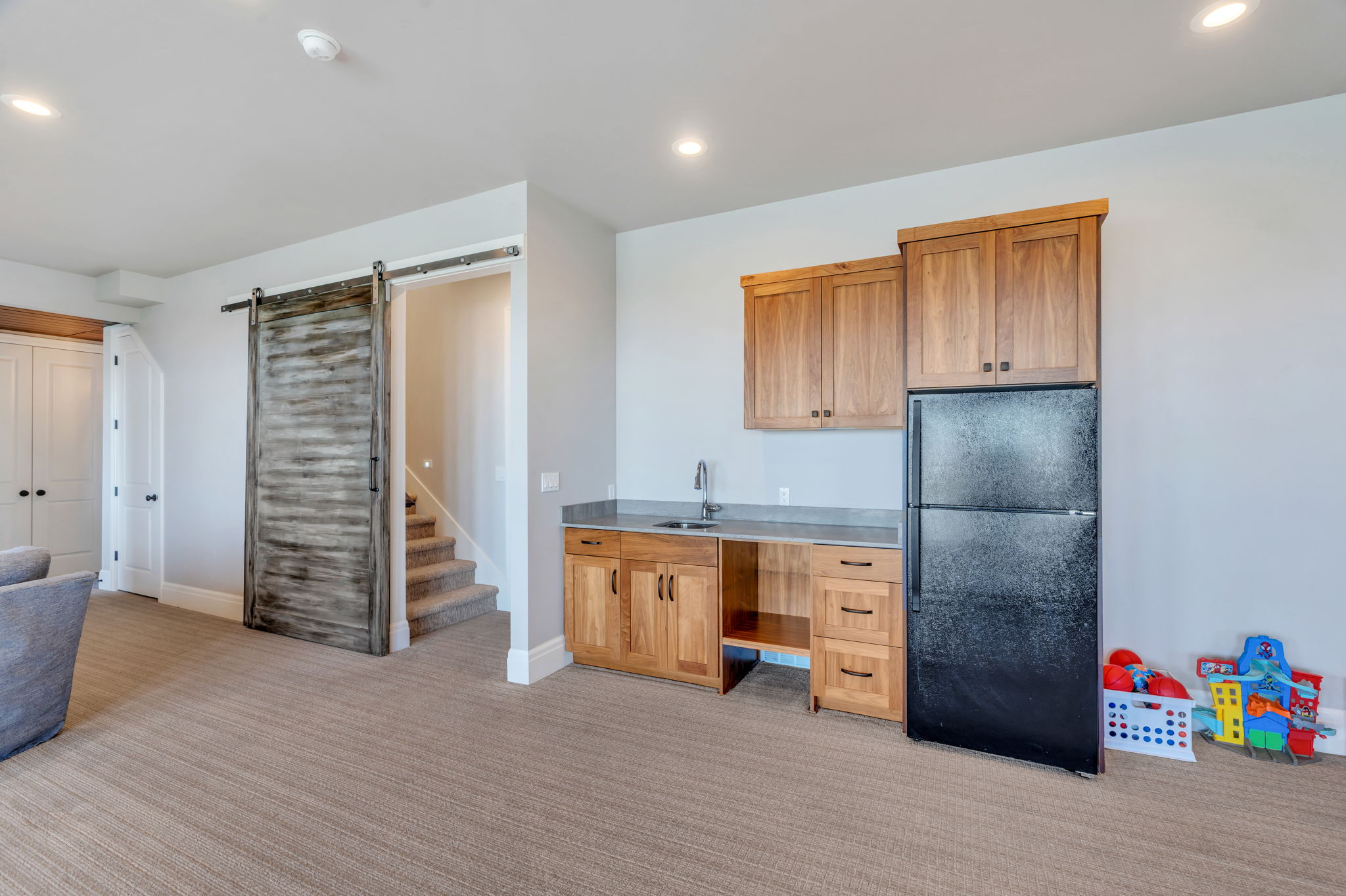 Contemporary wet bar featuring wood cabinetry, a stainless steel sink, and a black refrigerator