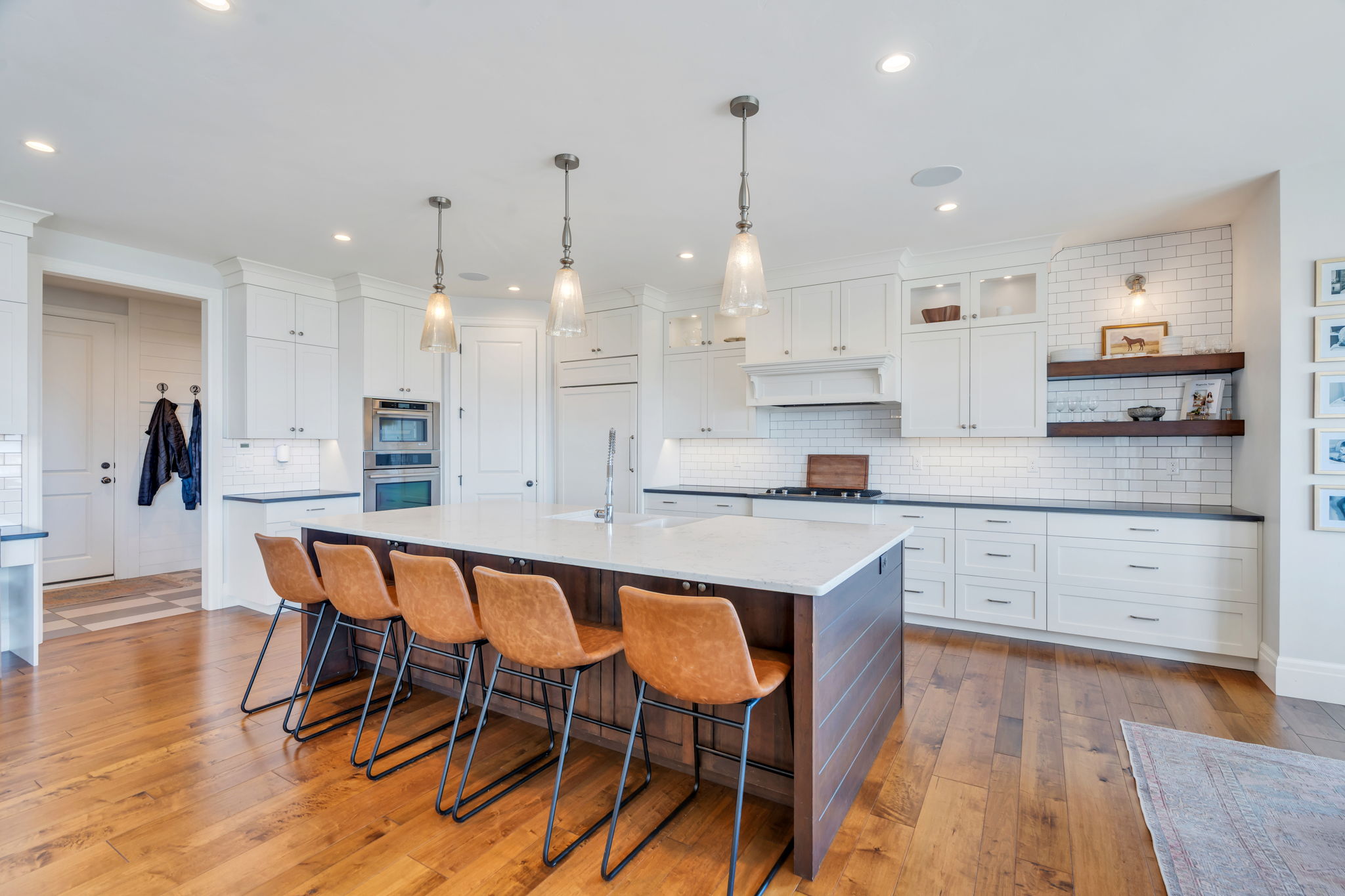 Spacious kitchen featuring a large central island with seating, white cabinetry, dark countertops, and a subway tile backsplash