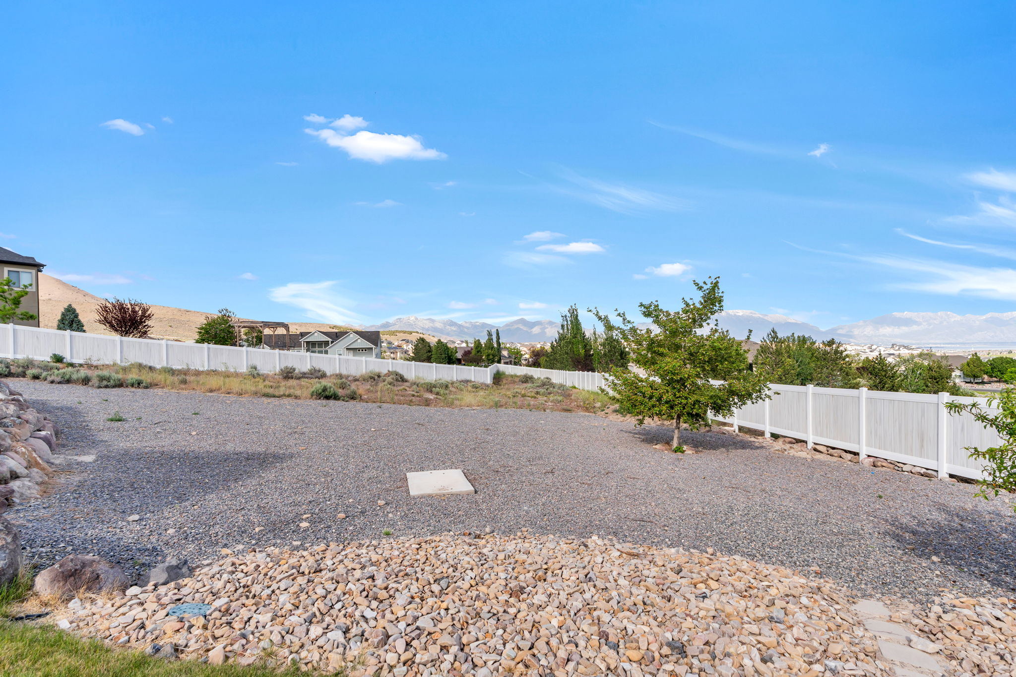 Expansive rear yard featuring gravel landscaping, a white privacy fence, and a mature tree