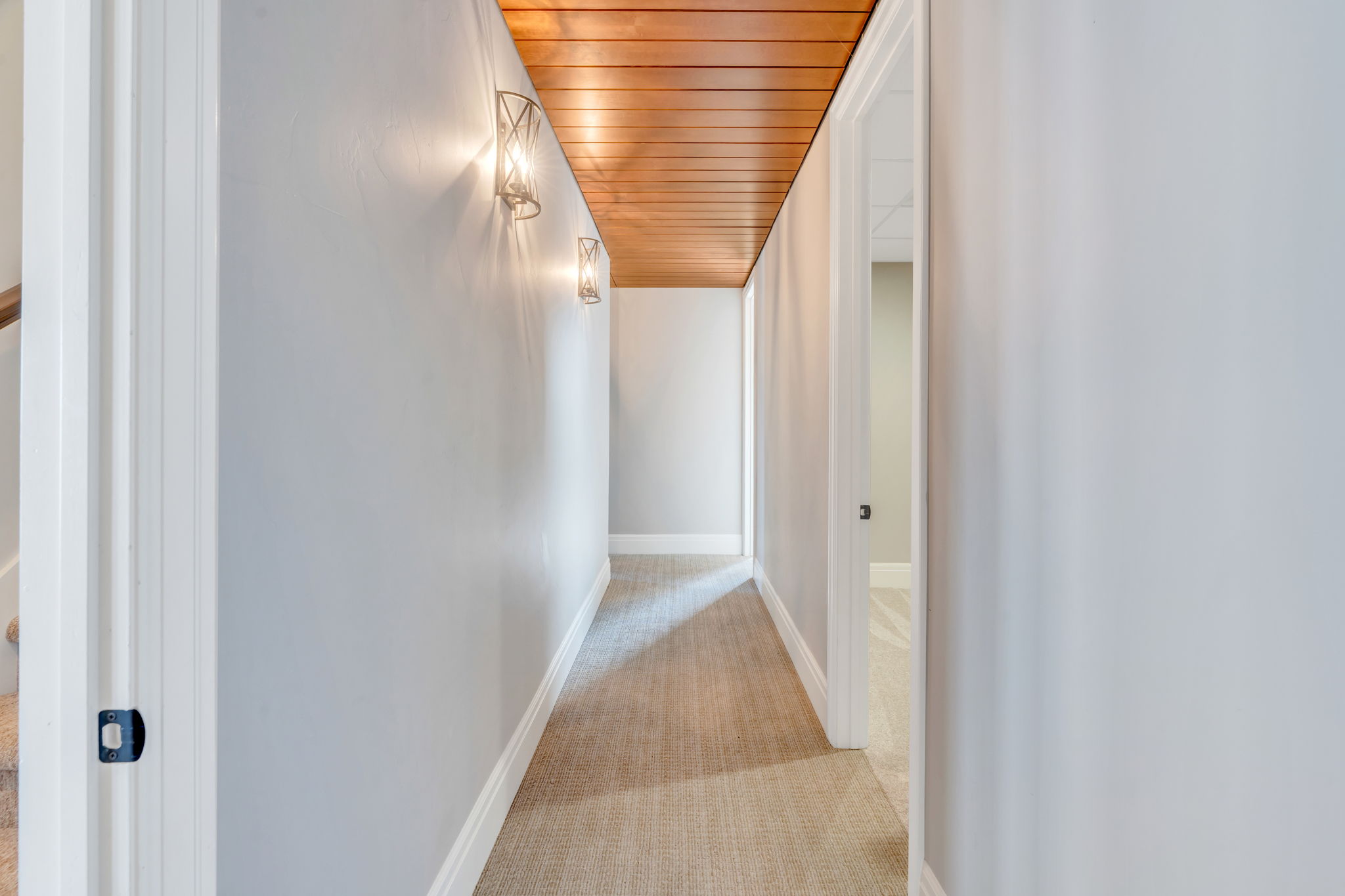 Hallway featuring a wood-panel ceiling, light gray walls, textured carpet flooring, and white baseboards