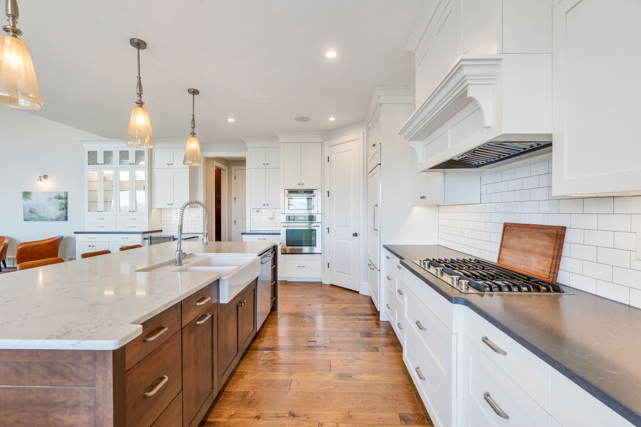 Gourmet kitchen featuring a large central island with an integrated farmhouse sink, quartz countertops, and wood-finish flooring