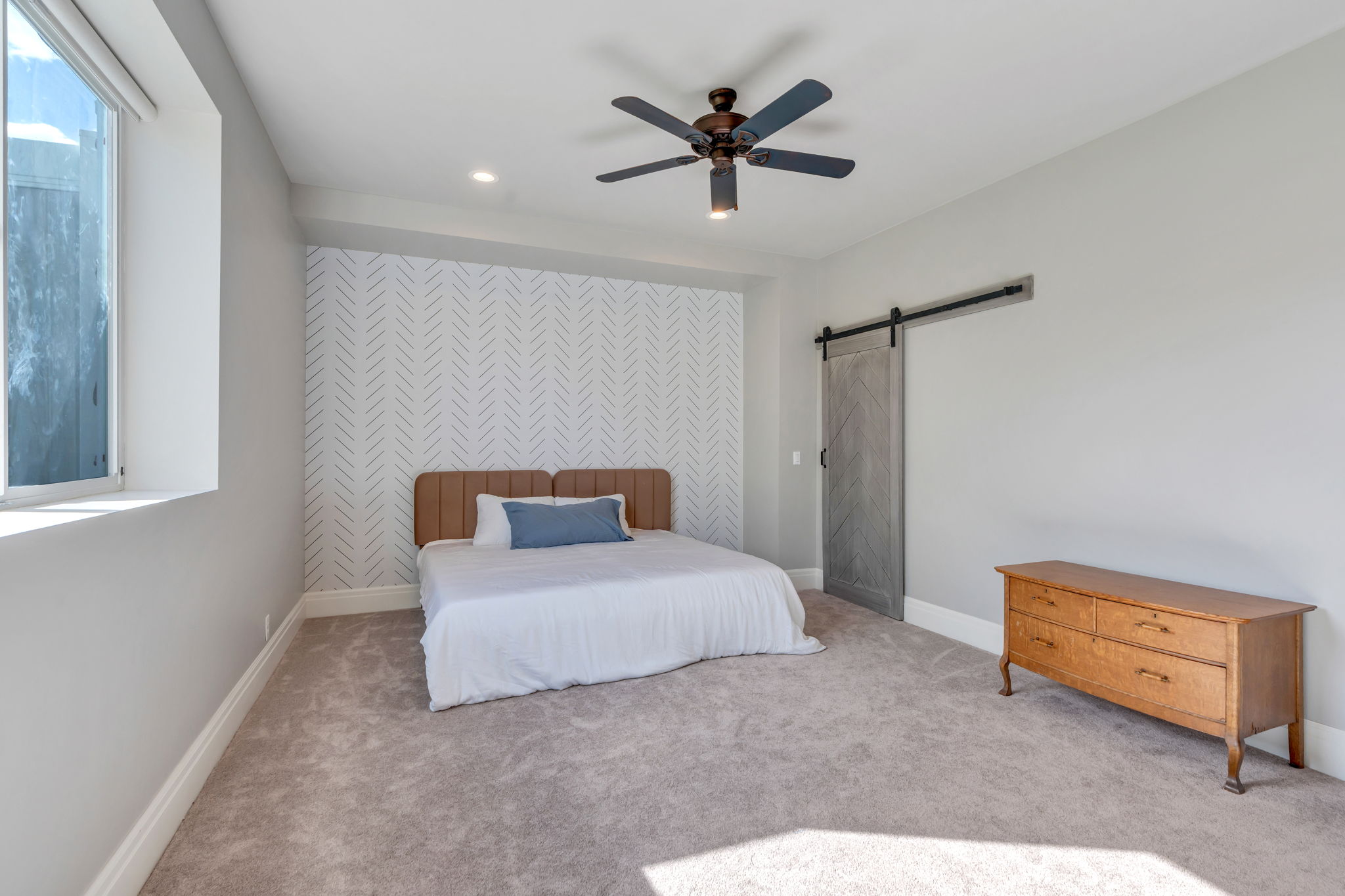Spacious room featuring light-colored carpeting, a textured accent wall, and a window with a roller shade