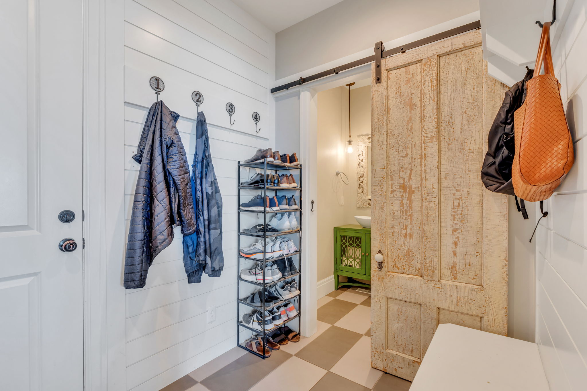 Mudroom entry featuring white shiplap wall paneling with numbered coat hooks, a weathered barn door, and checkered tile flooring
