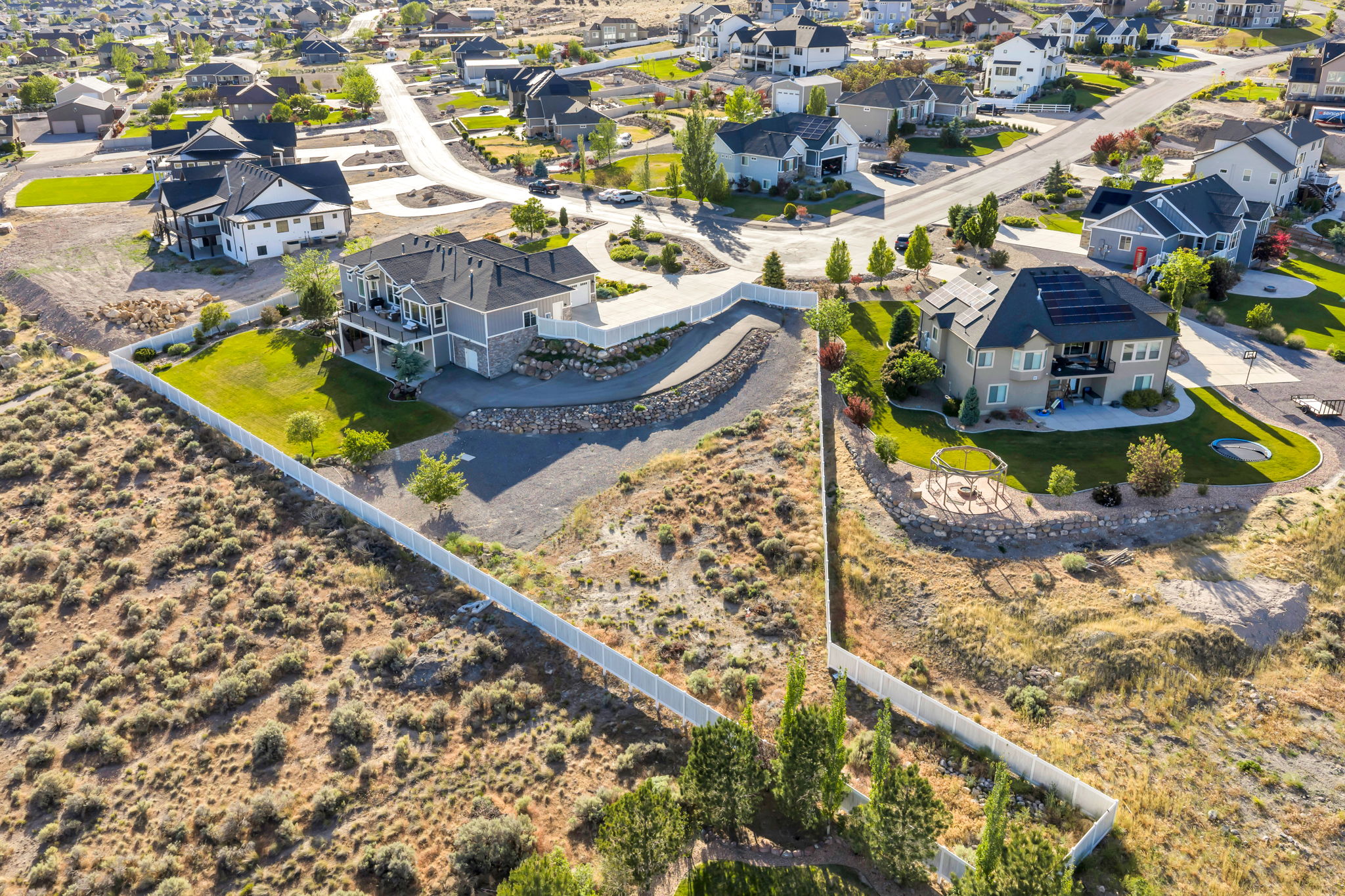 Expansive property with a white perimeter fence, featuring a paved driveway, mature trees, and a landscaped lawn area