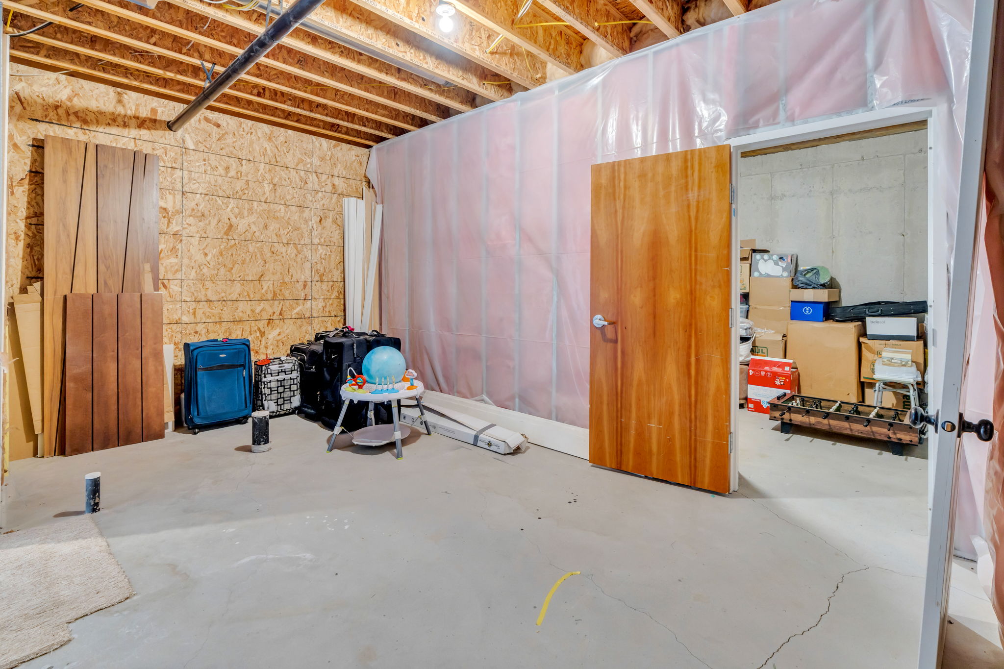 Unfinished basement area featuring exposed ceiling joists, concrete flooring, and a wood-paneled door
