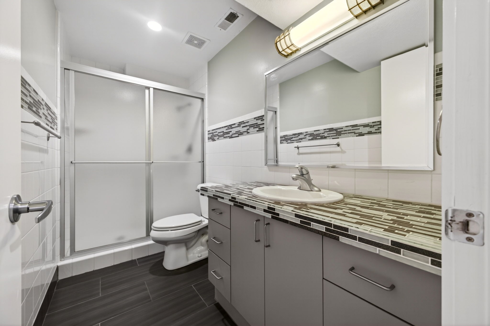 Bathroom featuring vanity with ample storage, a countertop with decorative tile inlay, a wall-mounted medicine cabinet, and contemporary gray floor.