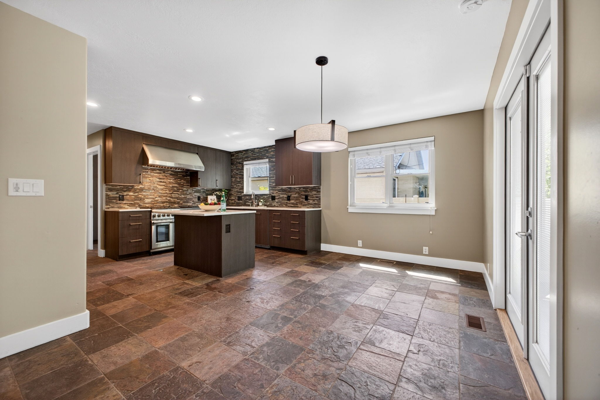 Open-concept kitchen and dining area featuring large window, slate flooring, and neutral toned walls