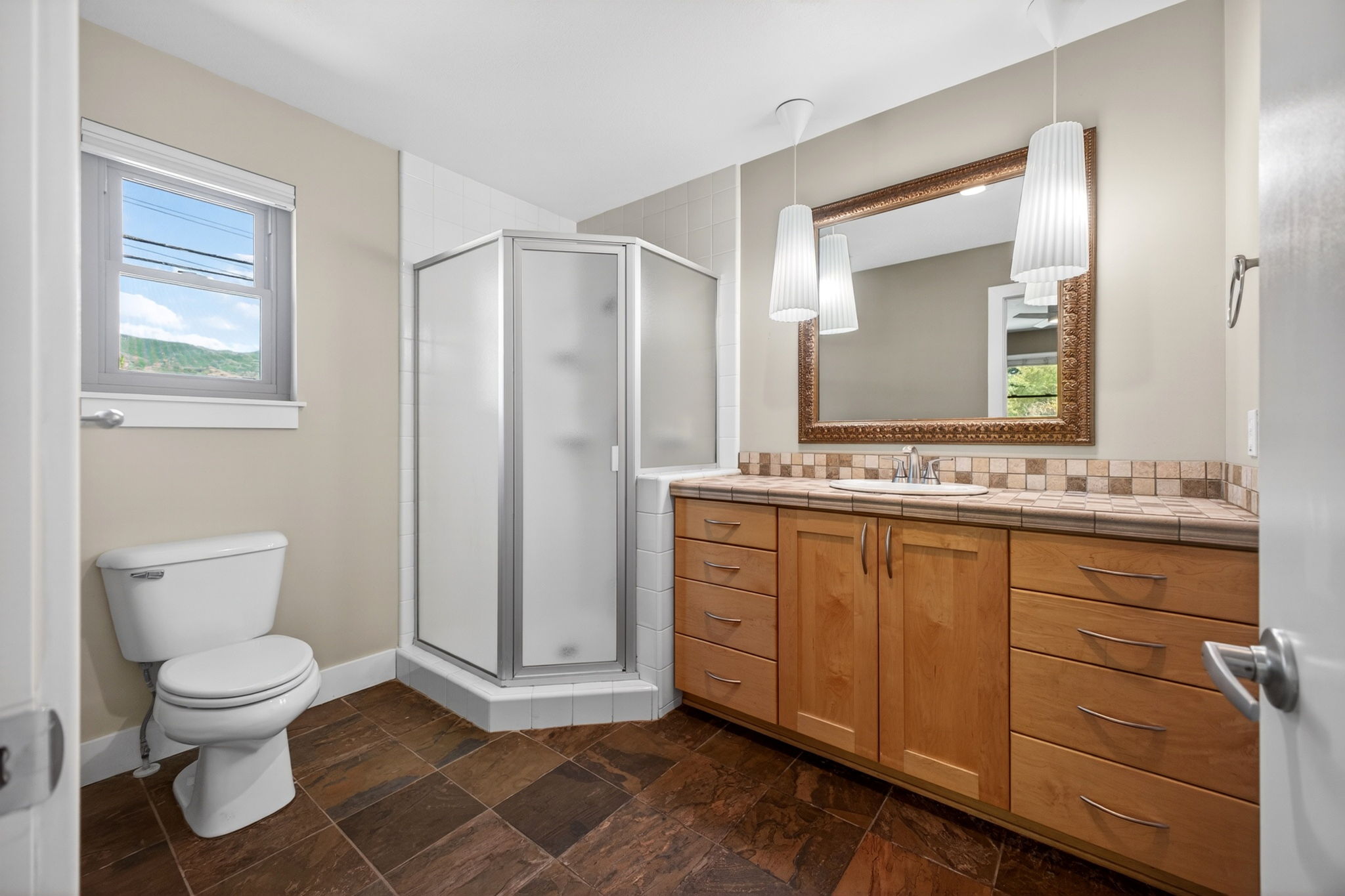 Ensuite bathroom featuring a wood-finish vanity with an integrated sink, tile countertop, and decorative mirror