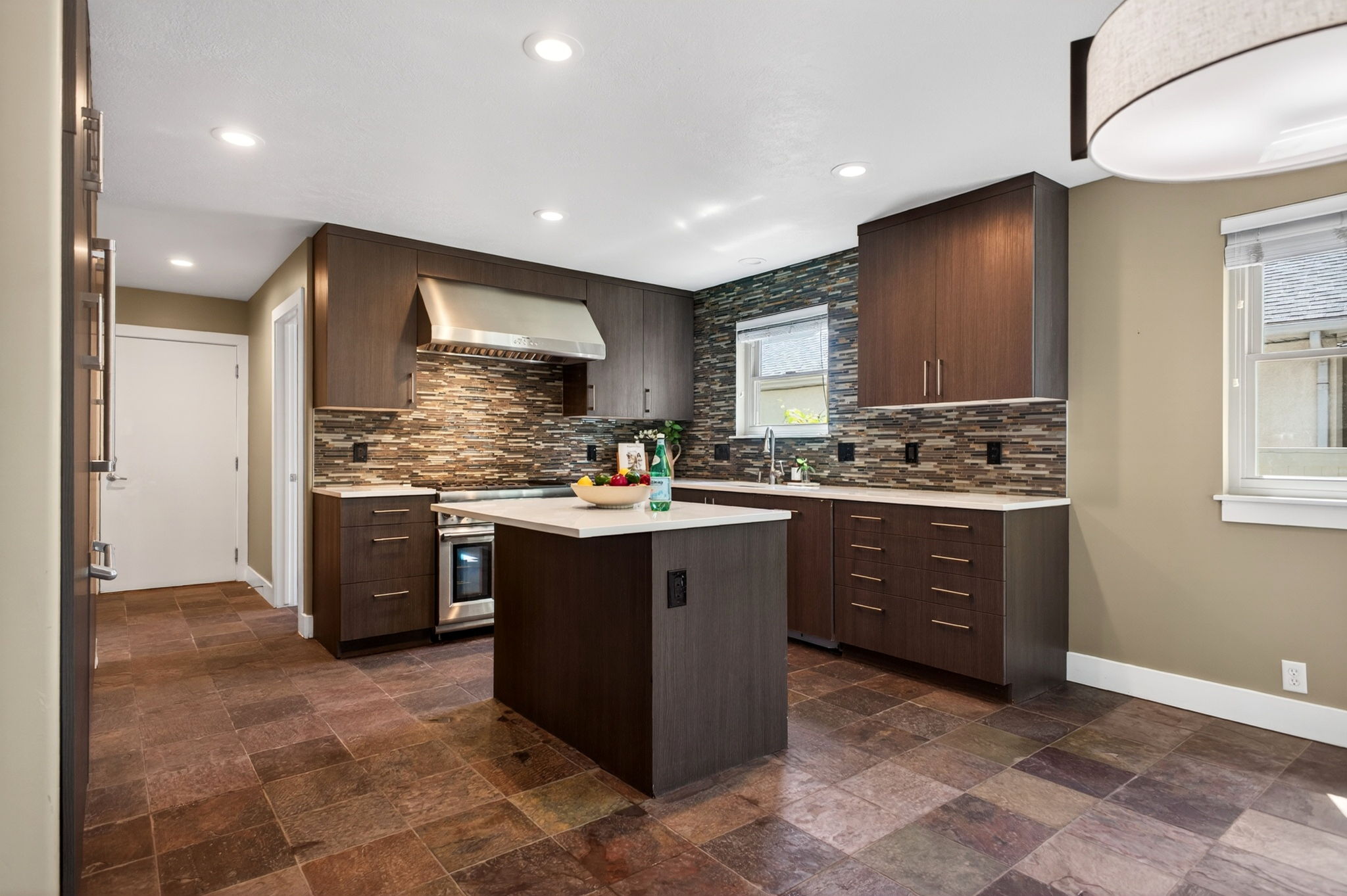 Spacious kitchen featuring an island, integrated stainless-steel appliances, dark wood-finish cabinetry, and slate tile flooring