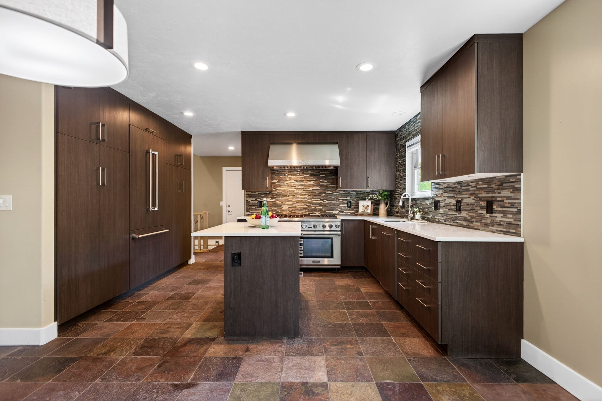 Kitchen featuring stainless steel appliances, a multi-tone tile backsplash, ample counter space, and a center island with white countertops