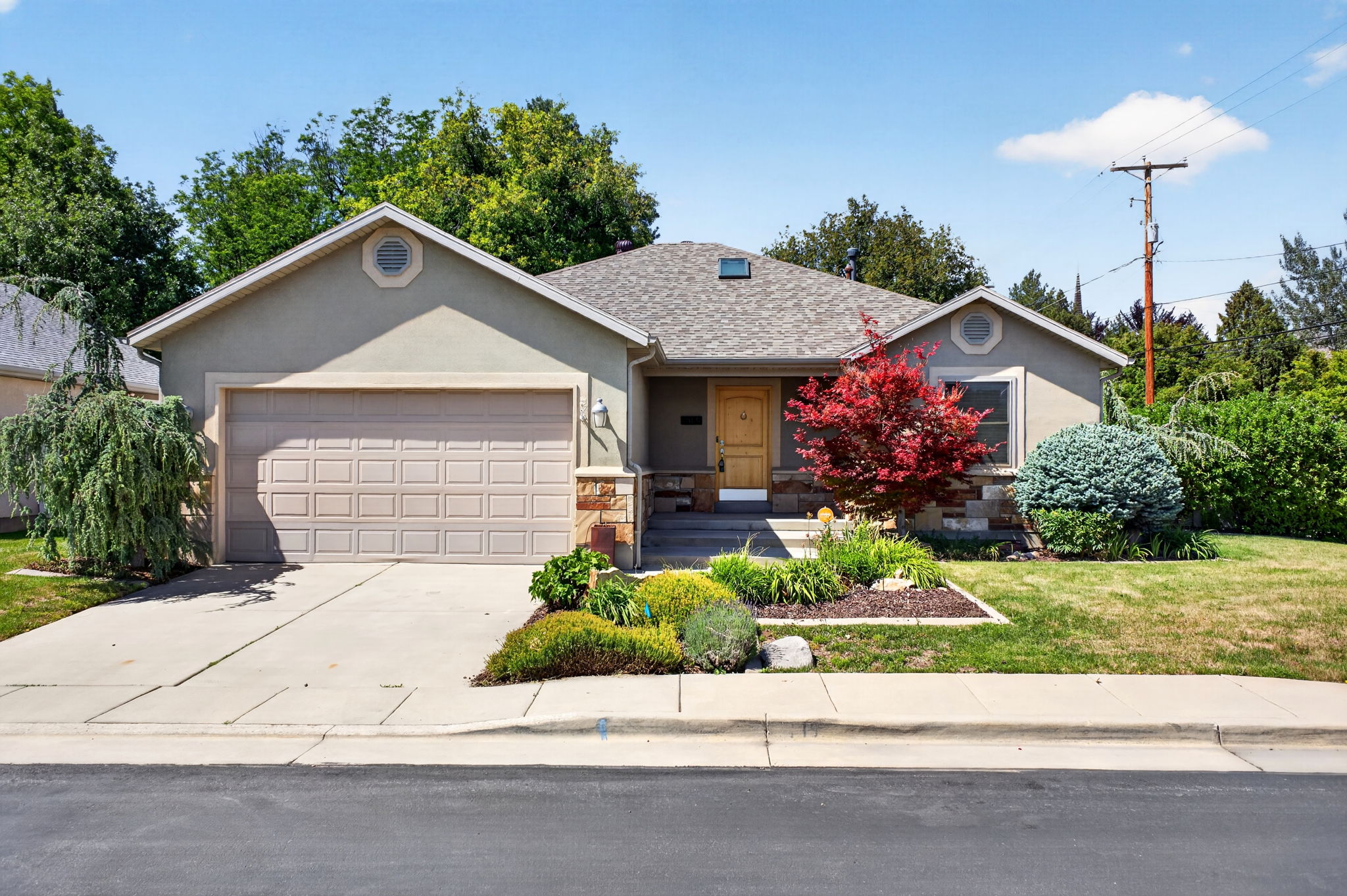 Stucco exterior with a two-car garage, concrete driveway, and front mature landscaping