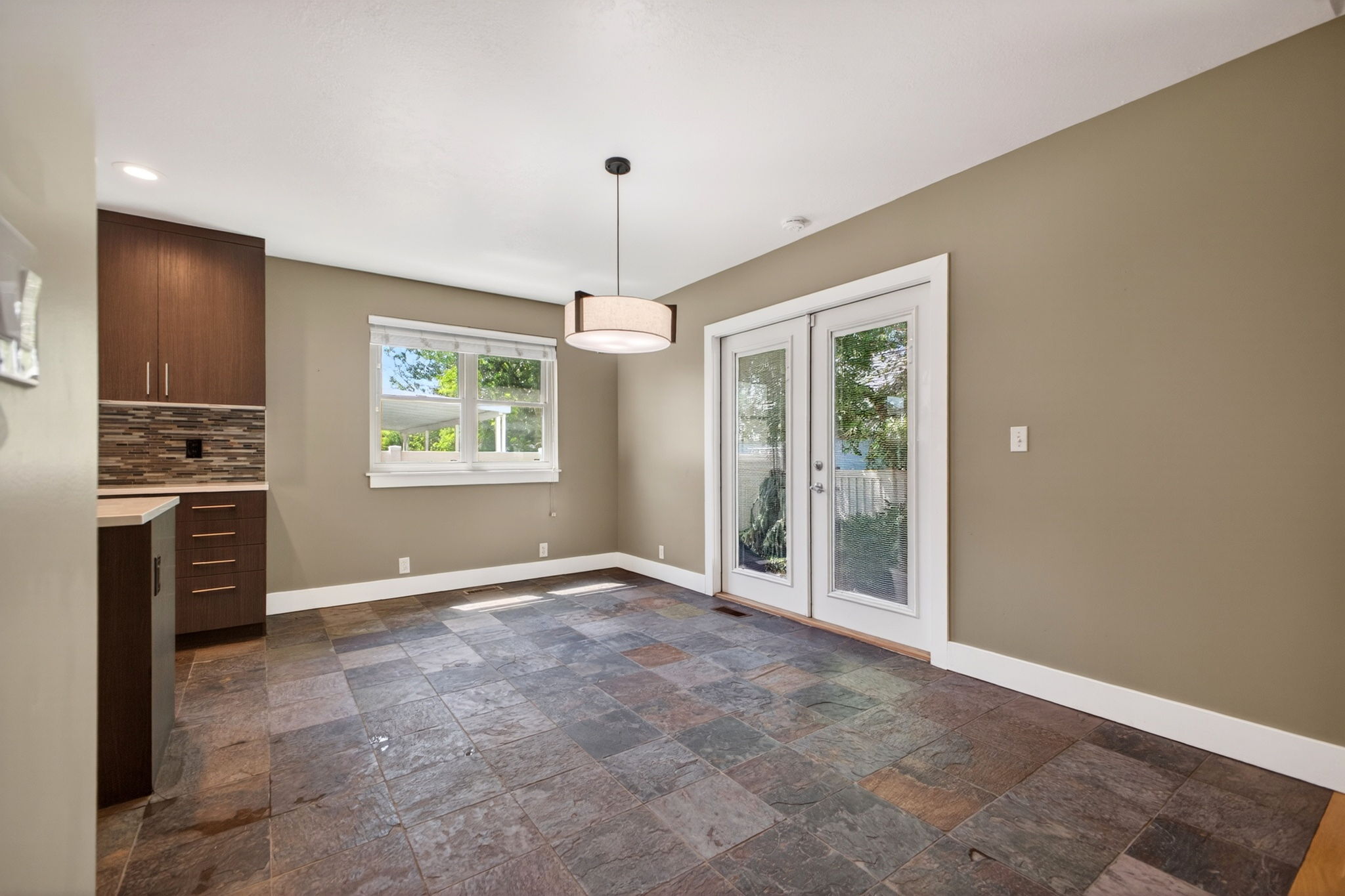 Dining area featuring slate tile flooring, French doors to the backyard, and a modern light fixture