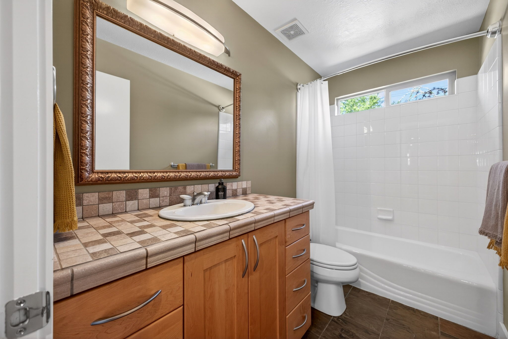 Full bathroom with light wood vanity, tiled countertop, and an oval sink