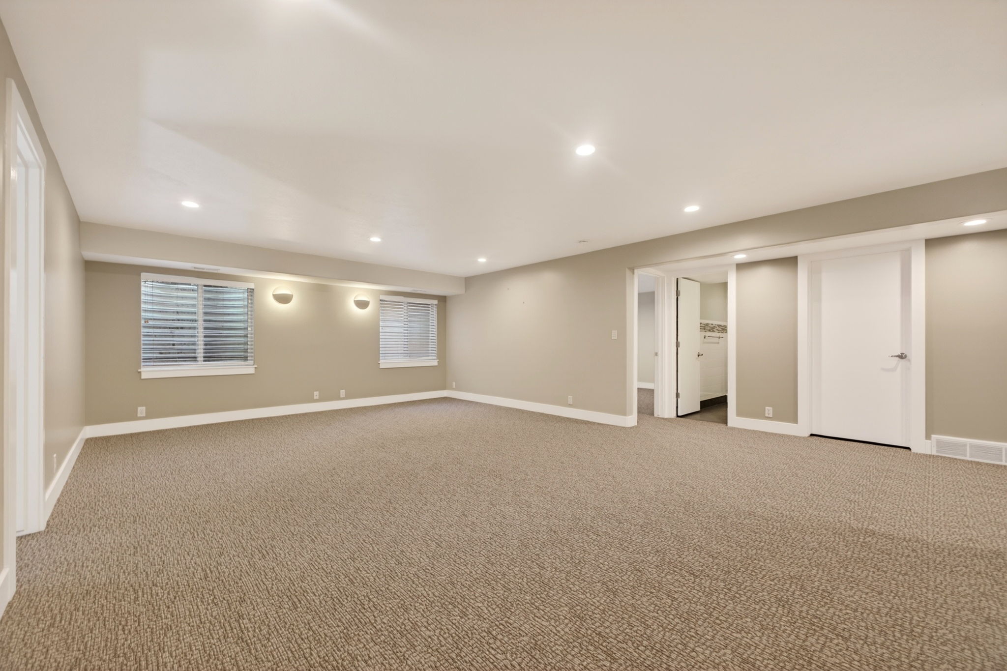 Large family room with modern sconces, two windows, and recessed lighting