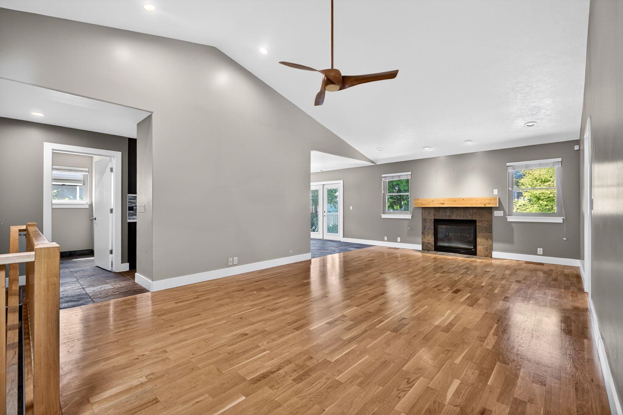 Spacious living area with a vaulted ceiling, fan, recessed lighting, and a fireplace with a stone surround and wood mantle