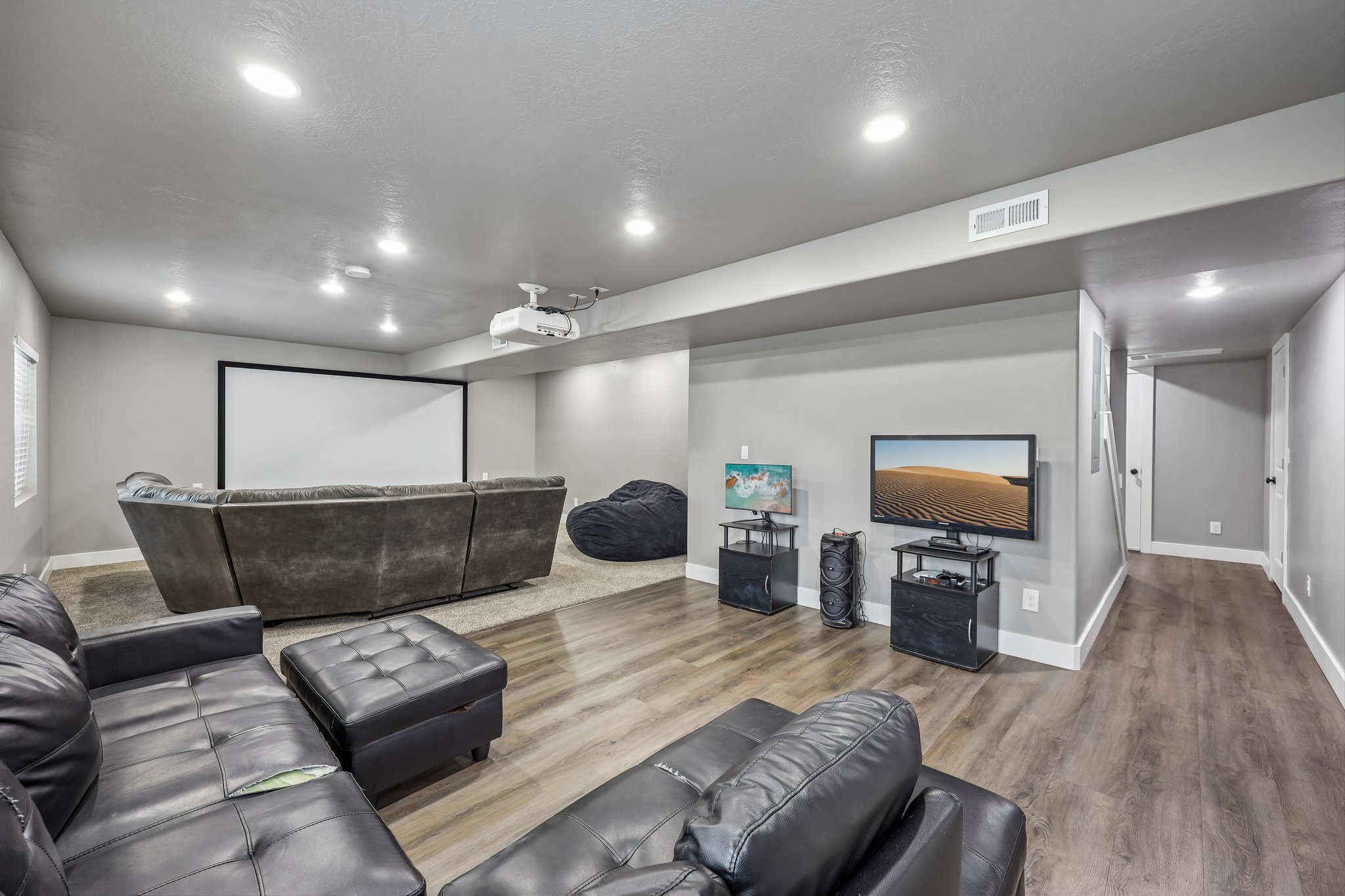 Dedicated entertainment space featuring a large projection screen, recessed lighting, and wood-finish flooring