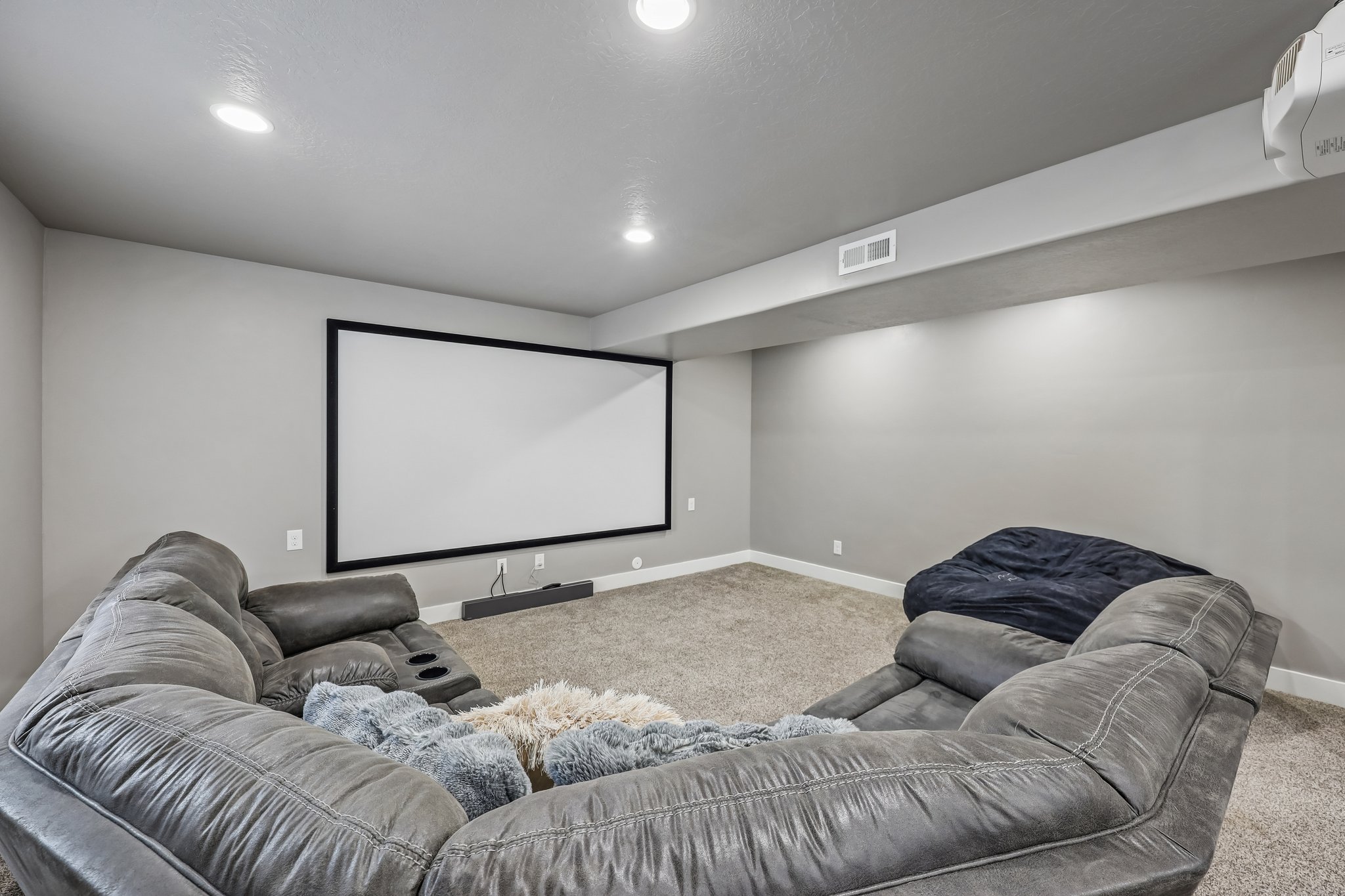 Dedicated media room featuring a large projection screen, recessed ceiling lighting, and wall-mounted projector