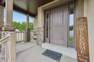 Inviting front porch featuring a paneled entry door with sidelights, stone-clad pillars, a wood-finish ceiling, and a concrete patio