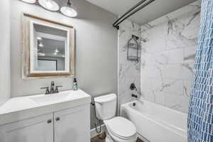 Bathroom featuring a white vanity with integrated sink, a distressed wood-frame mirror, a three-light vanity fixture, a white toilet, and a white bathtub with marble-look tile surround