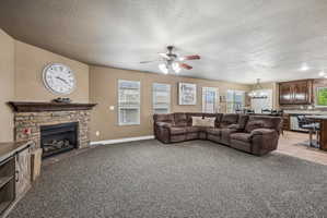 Spacious living area featuring a stone-clad fireplace with a wood mantel, carpet flooring, a ceiling fan, and multiple windows with blinds