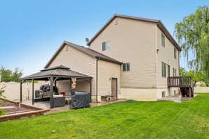 Spacious backyard featuring a covered patio structure, a raised garden bed with stone surround, a wood deck with stairs, a privacy fence, and mature trees
