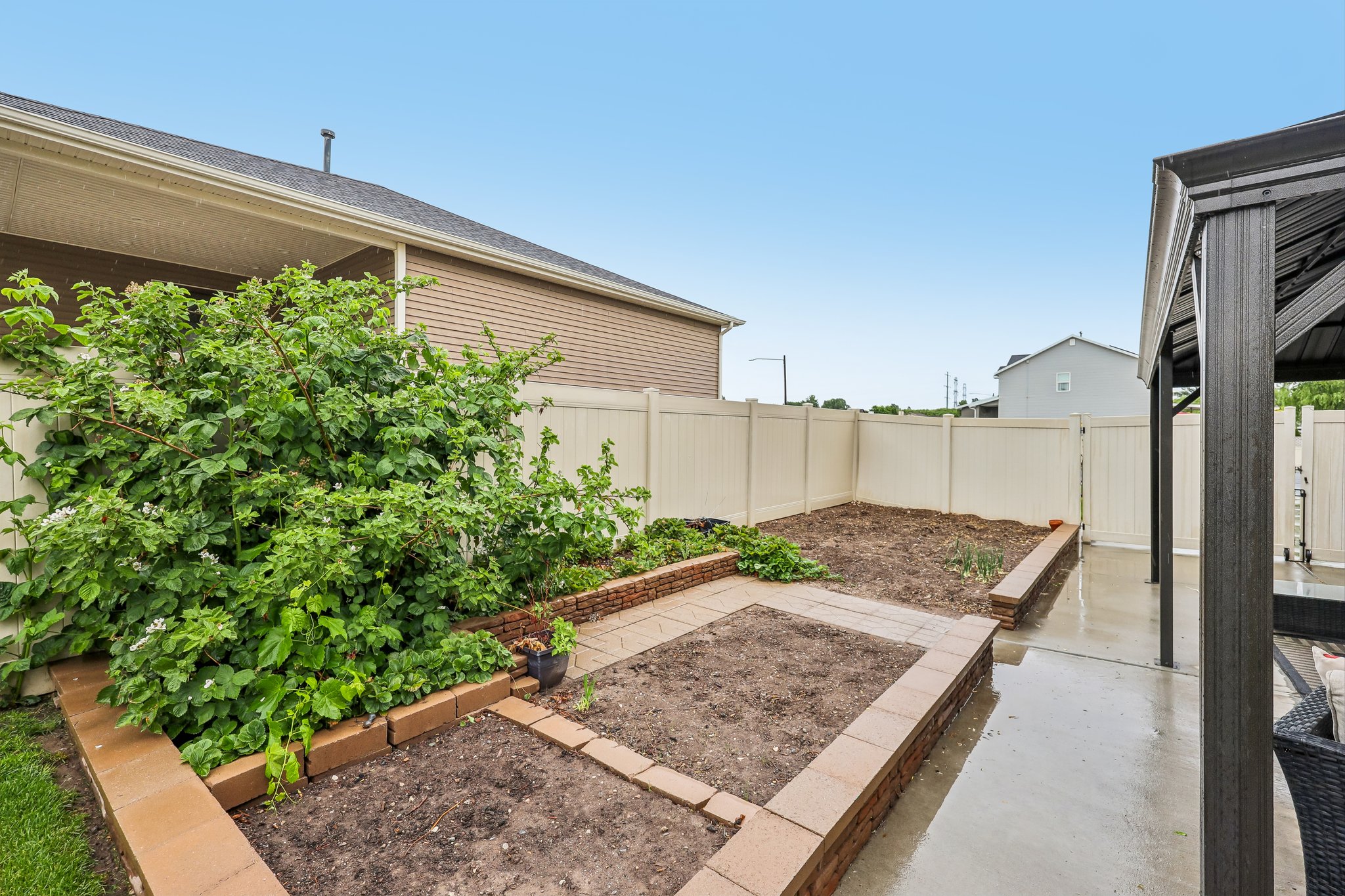Rear yard featuring a privacy fence, concrete patio, and raised garden beds with brick-style retaining walls