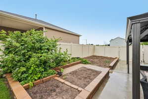 Rear yard featuring a privacy fence, concrete patio, and raised garden beds with brick-style retaining walls