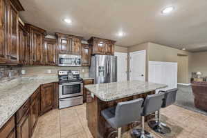 Kitchen featuring granite countertops, wood cabinetry, stainless steel appliances, and a breakfast bar island