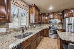 Kitchen featuring rich wood cabinetry, stone veneer backsplash, light granite countertops, and stainless steel appliances