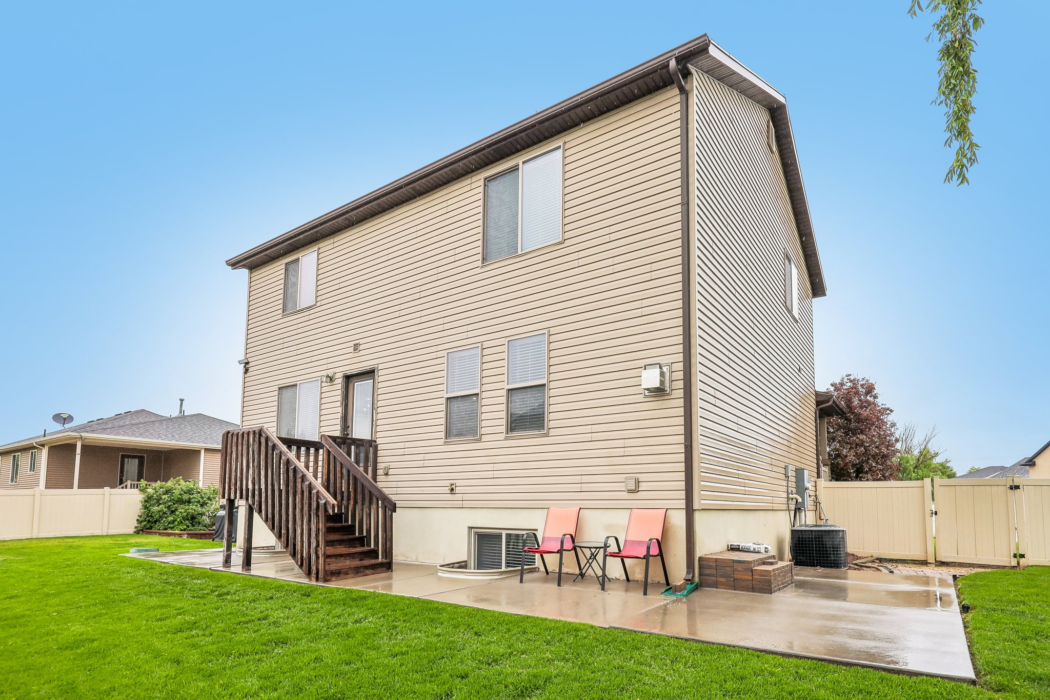 Expansive rear lawn featuring a concrete patio, wooden deck, and tan vinyl siding