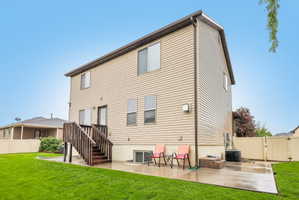 Expansive rear lawn featuring a concrete patio, wooden deck, and tan vinyl siding