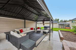 Covered patio featuring a solid roof structure, concrete flooring, and a raised brick garden bed