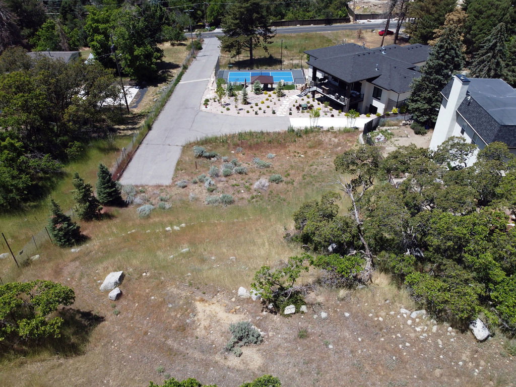 Expansive undeveloped lot featuring natural vegetation, scattered rocks, and mature trees, bordered by a paved road