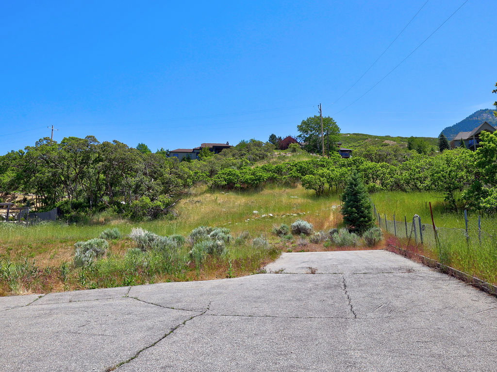 Paved surface with visible cracking, surrounded by natural vegetation and distant residential structures