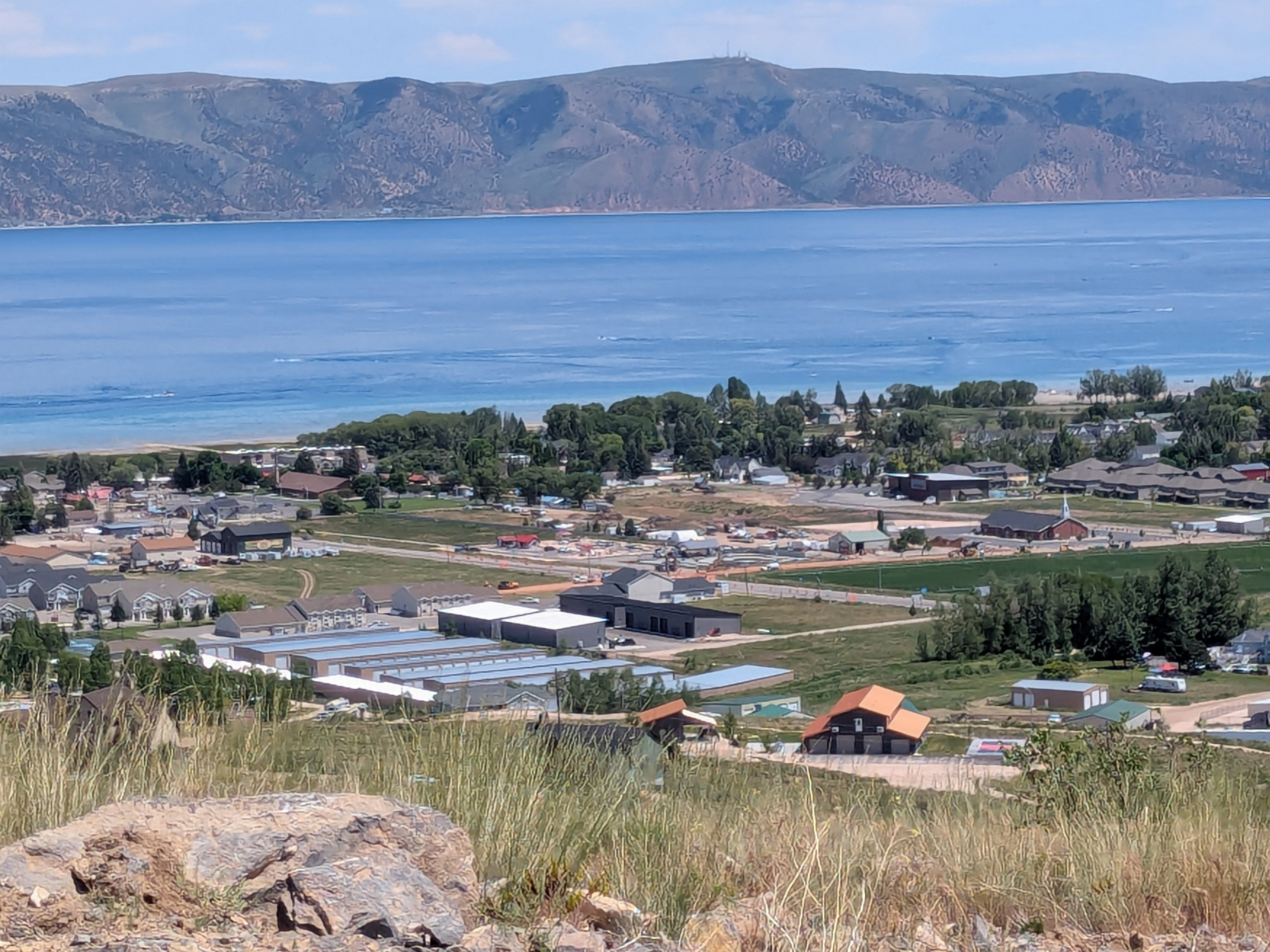 Panoramic landscape featuring expansive water frontage with distant mountains, a community shoreline, and varied architectural styles across the hillside