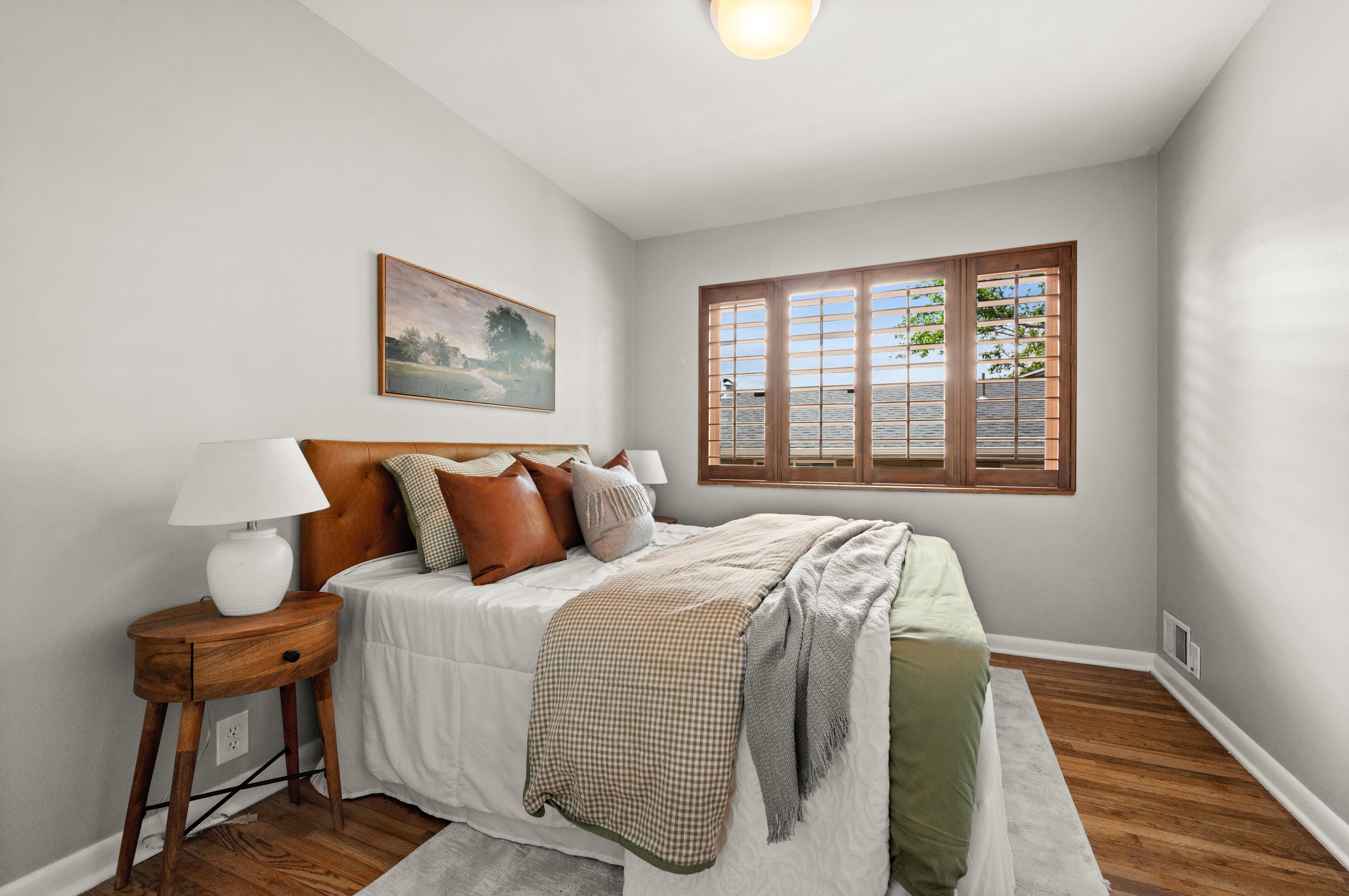 Bedroom featuring wood-finish flooring, light gray wall paint, and a window with custom wood plantation shutters