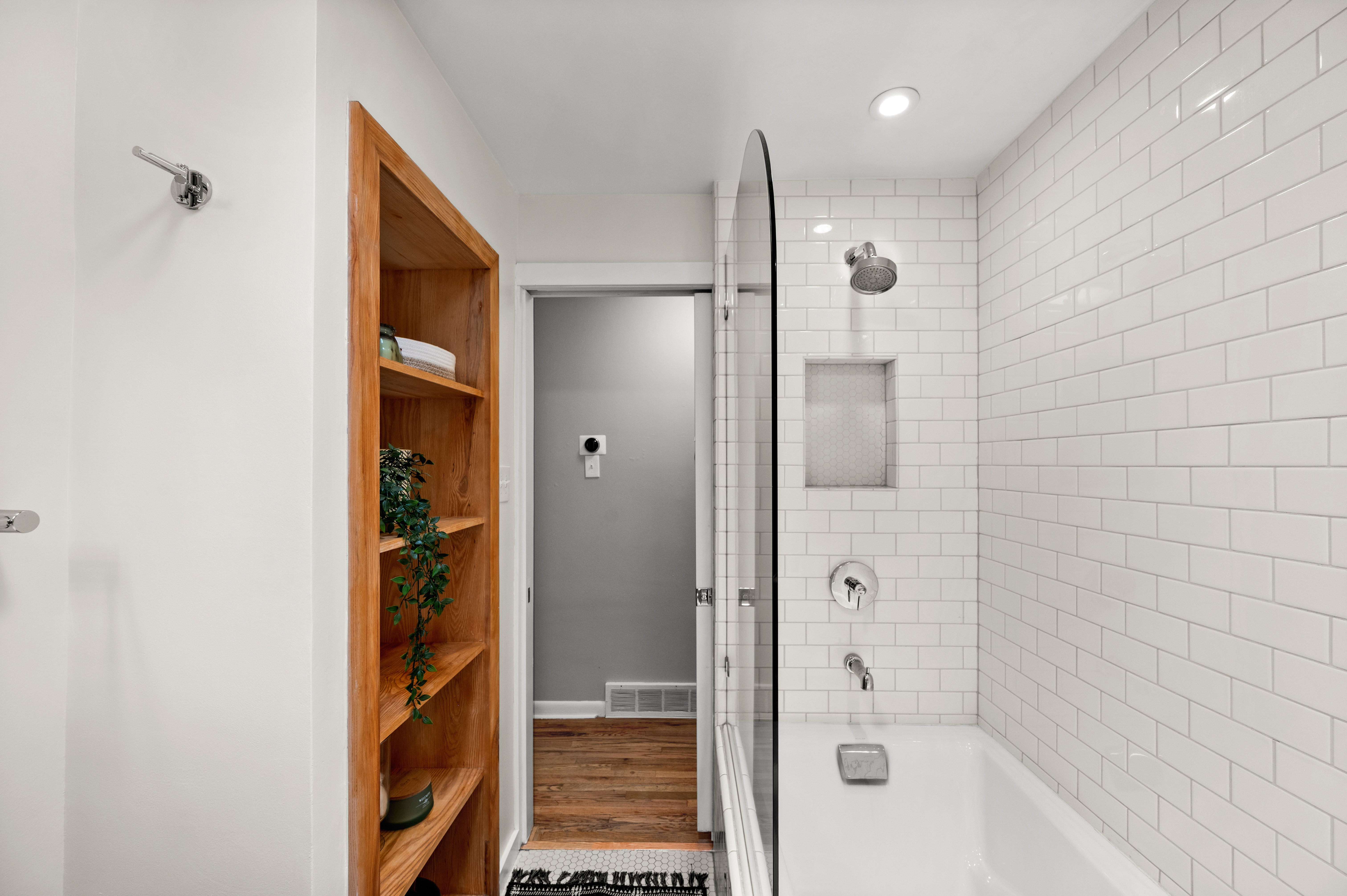 Tiled shower/tub combination with subway tile surround, recessed niche, and clear glass partition