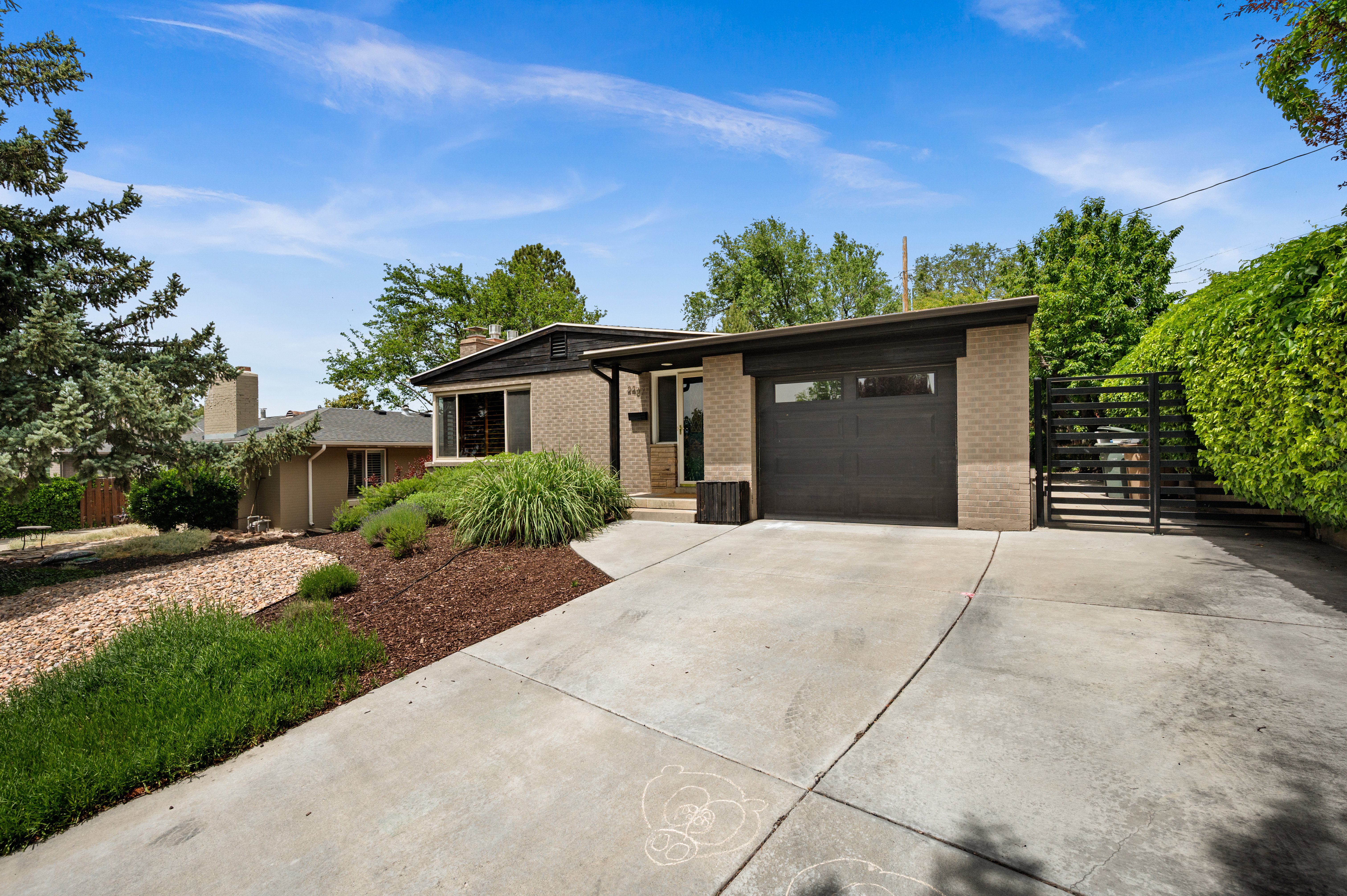 Brick exterior featuring a dark-toned garage door, concrete driveway, and established landscaping