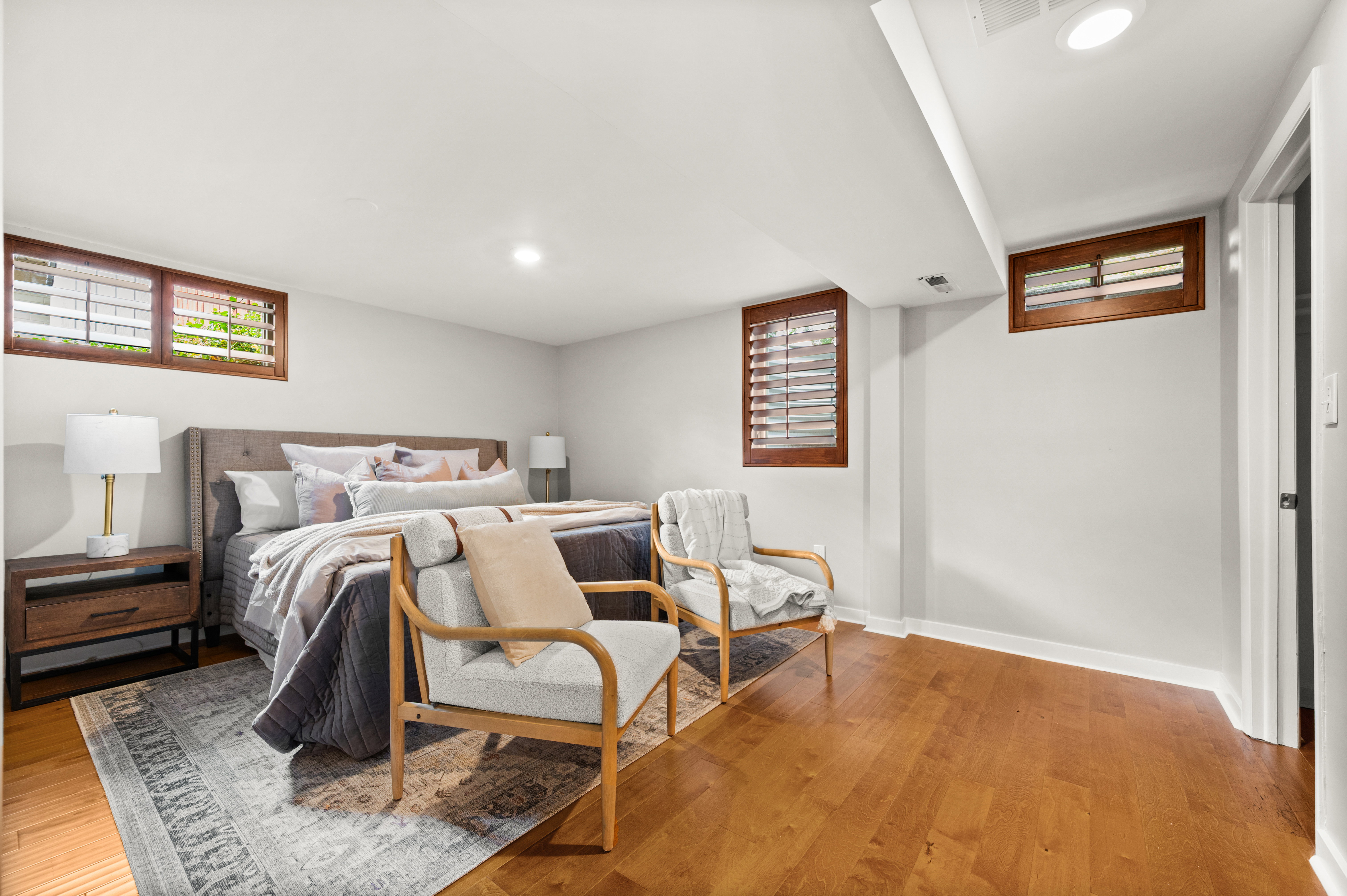 Spacious bedroom featuring wood-finish flooring, recessed lighting, and wall-mounted windows with wood shutters