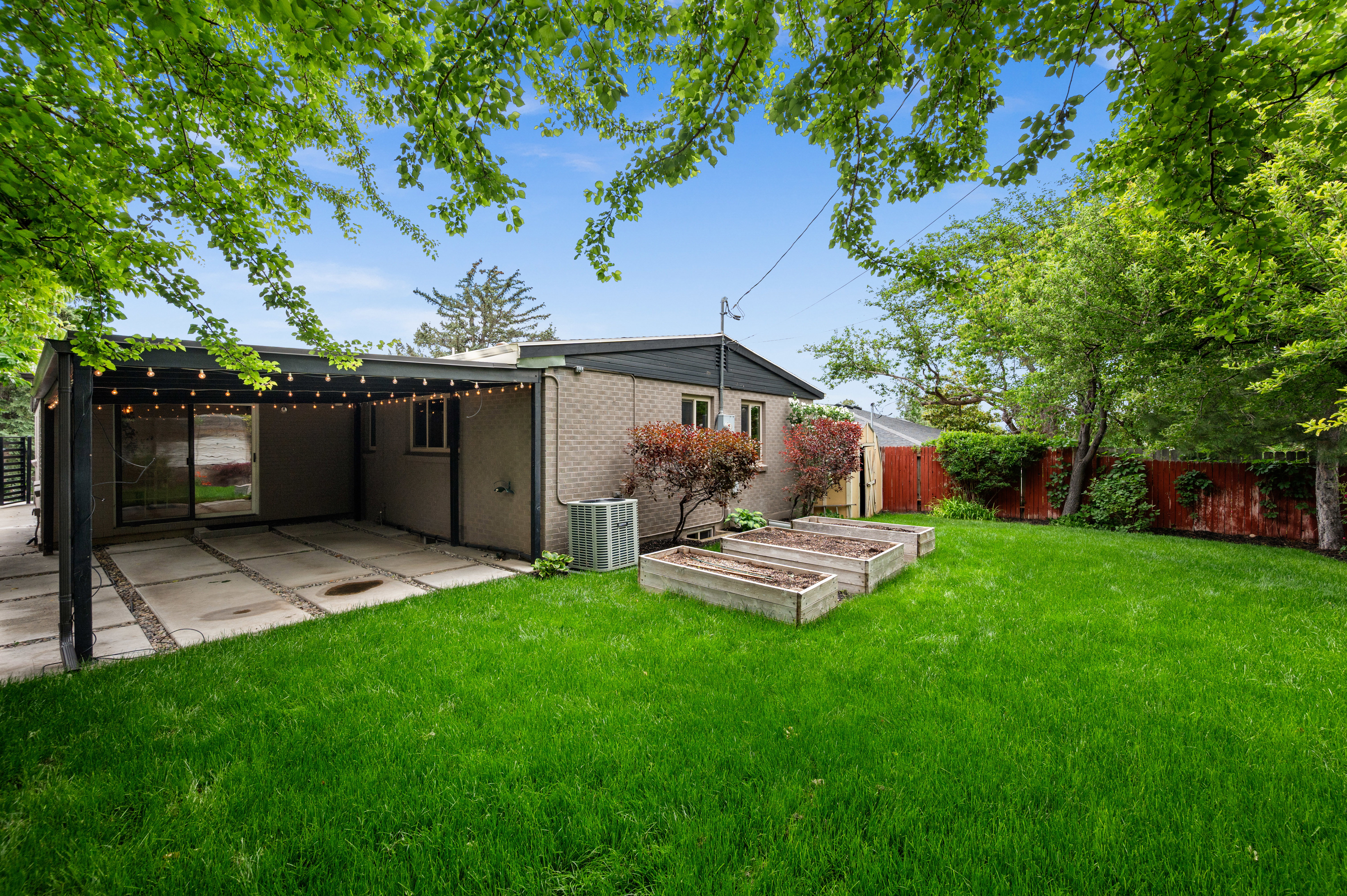 Expansive backyard featuring a manicured lawn, mature trees, and raised garden beds