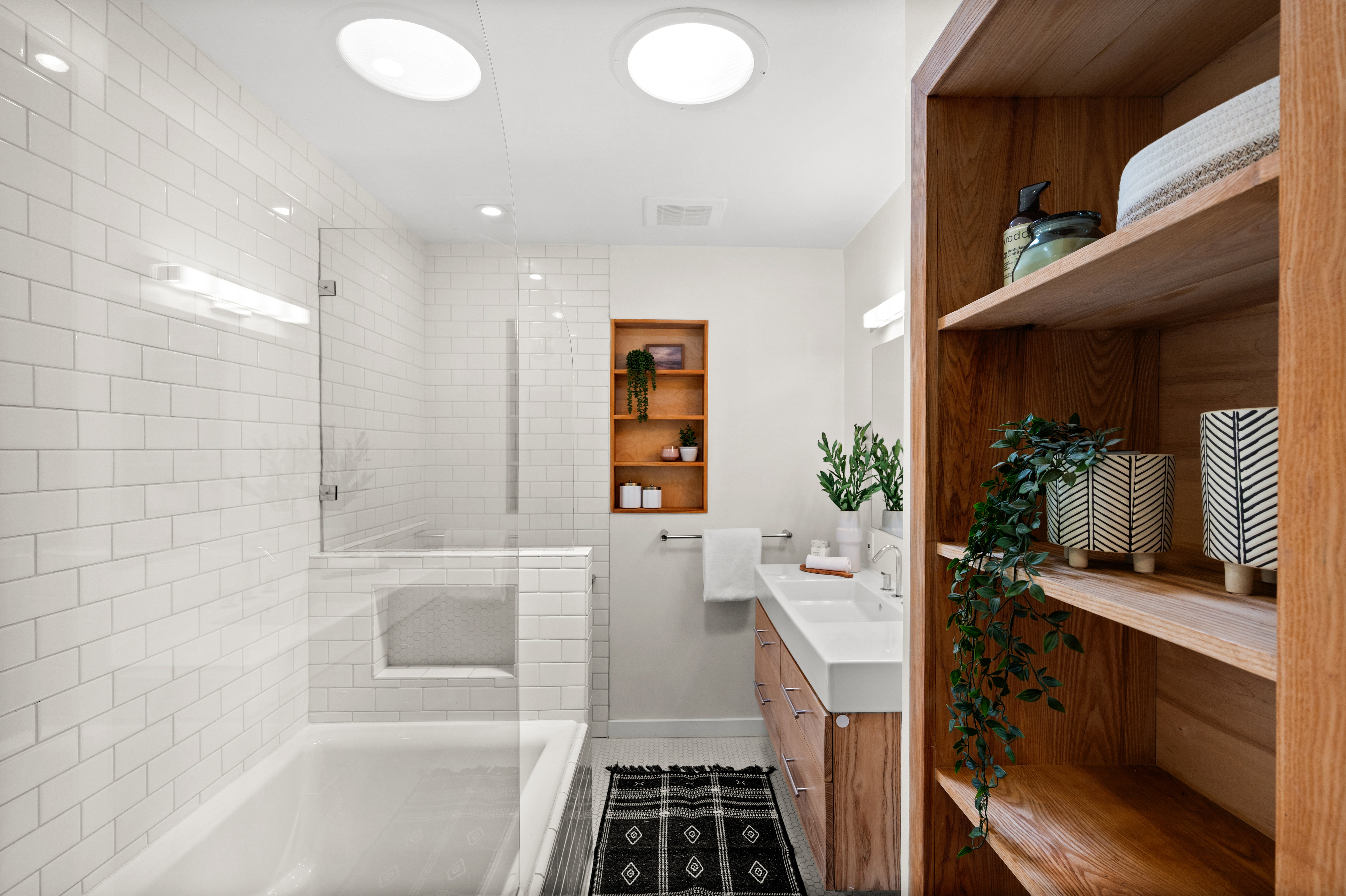 Bathroom featuring a tub and shower combination with glass enclosure, white subway tile surround, and recessed shelving