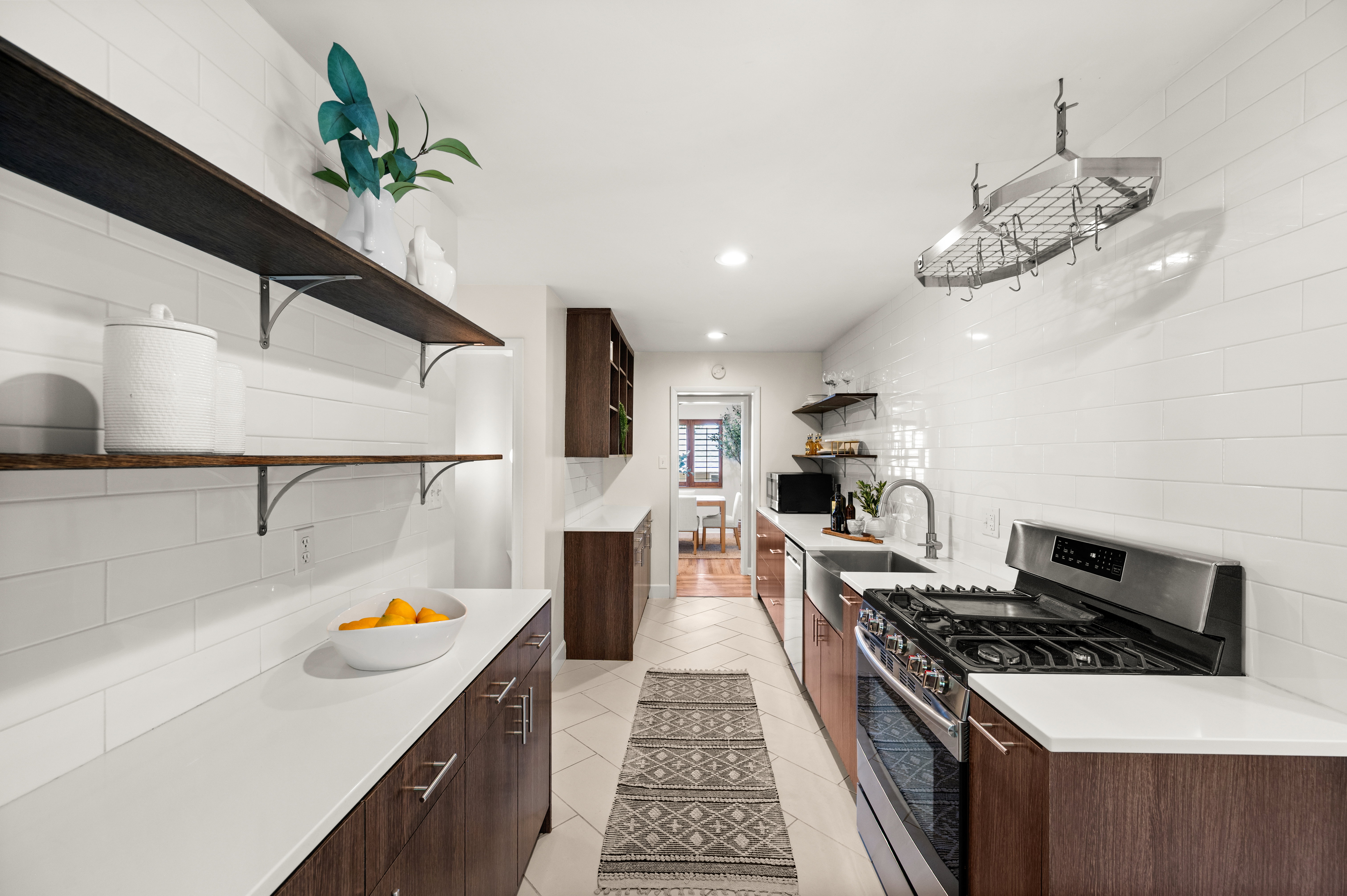 Galley kitchen featuring white subway tile backsplash, white countertops, wood-finish cabinetry, stainless steel appliances, and open shelving