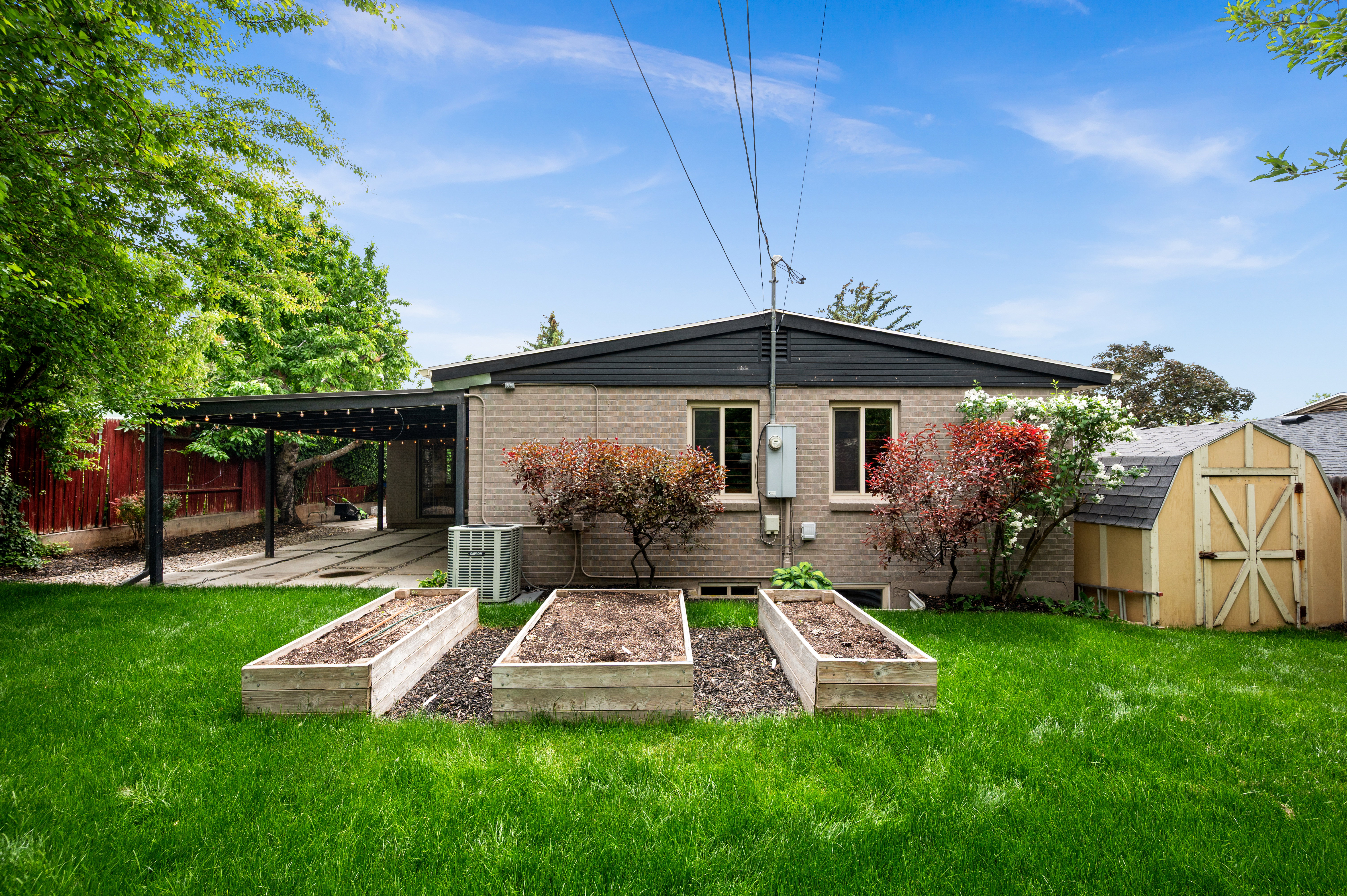 Expansive backyard featuring a manicured lawn, three raised garden beds, and a detached storage shed