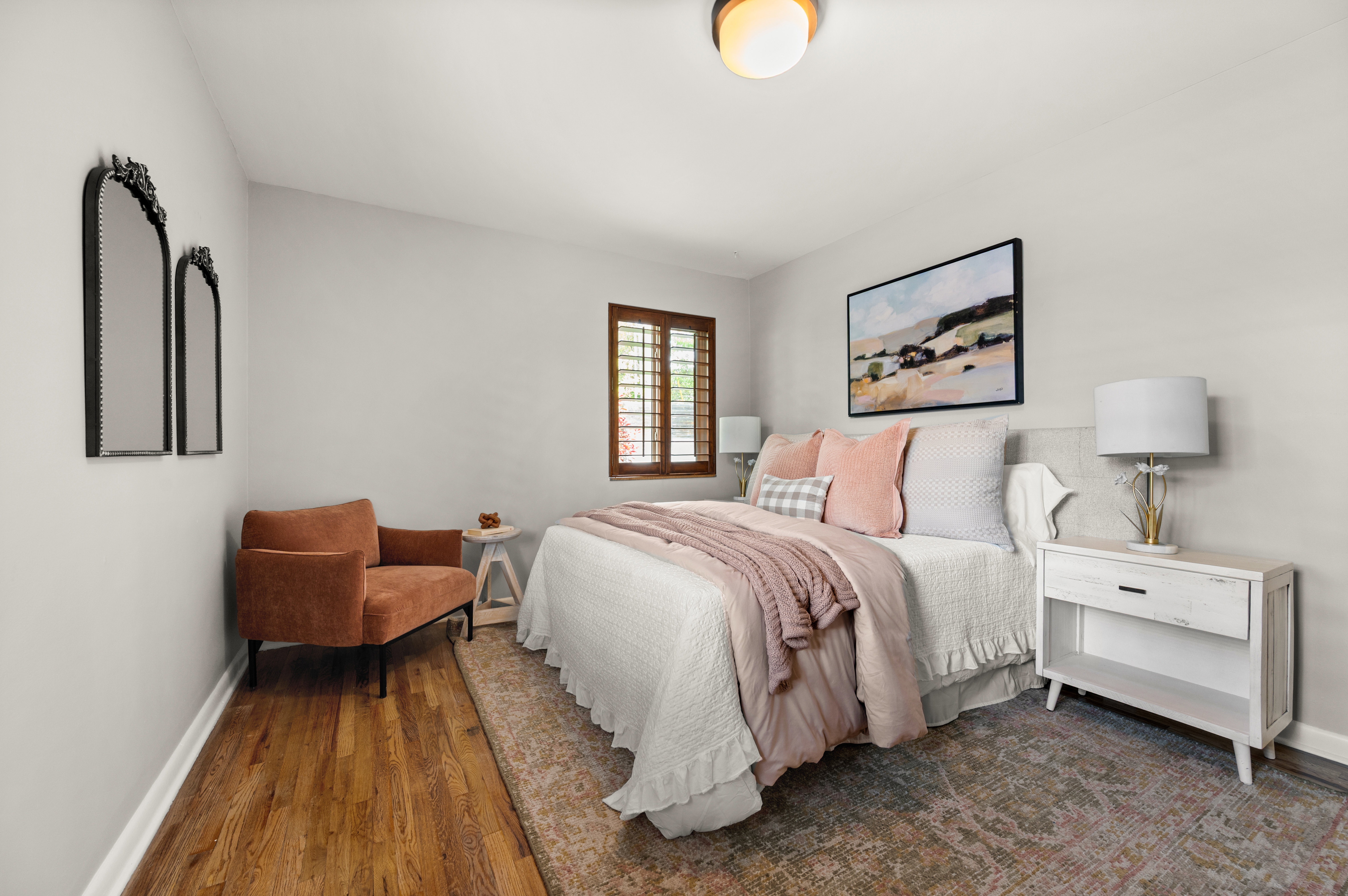 Bedroom featuring hardwood flooring, light gray walls, and a window with wood plantation shutters