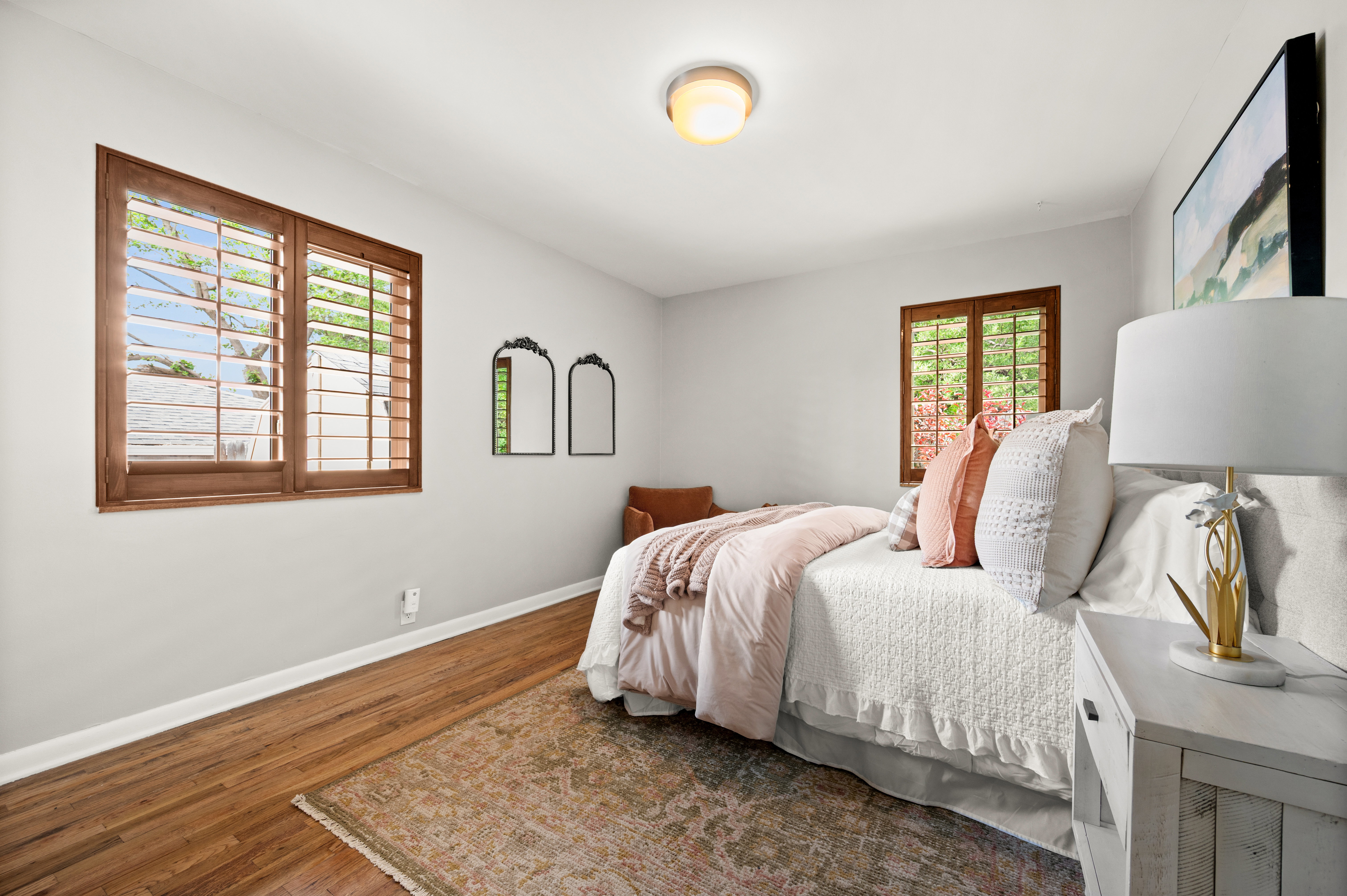 Bedroom with wood-finish flooring, white walls, and two windows featuring wooden plantation shutters